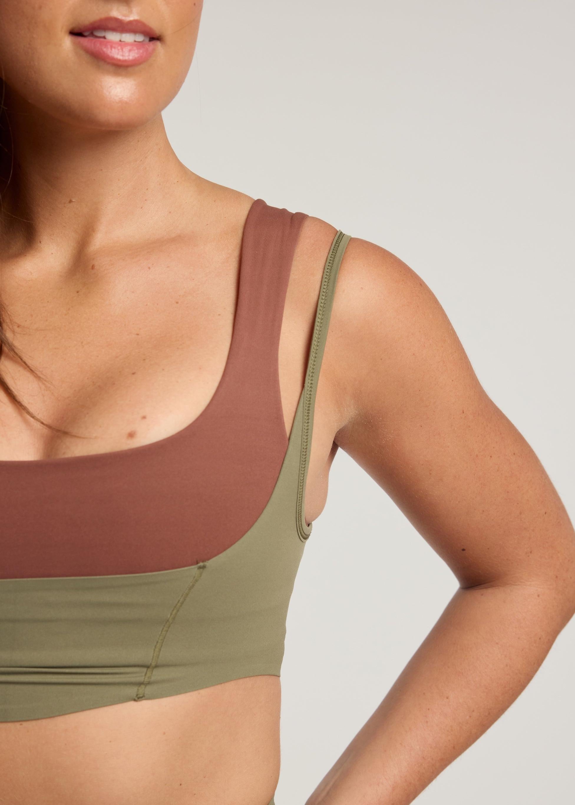 Person wearing a two-tone sports bra with brown and green colors on a neutral background