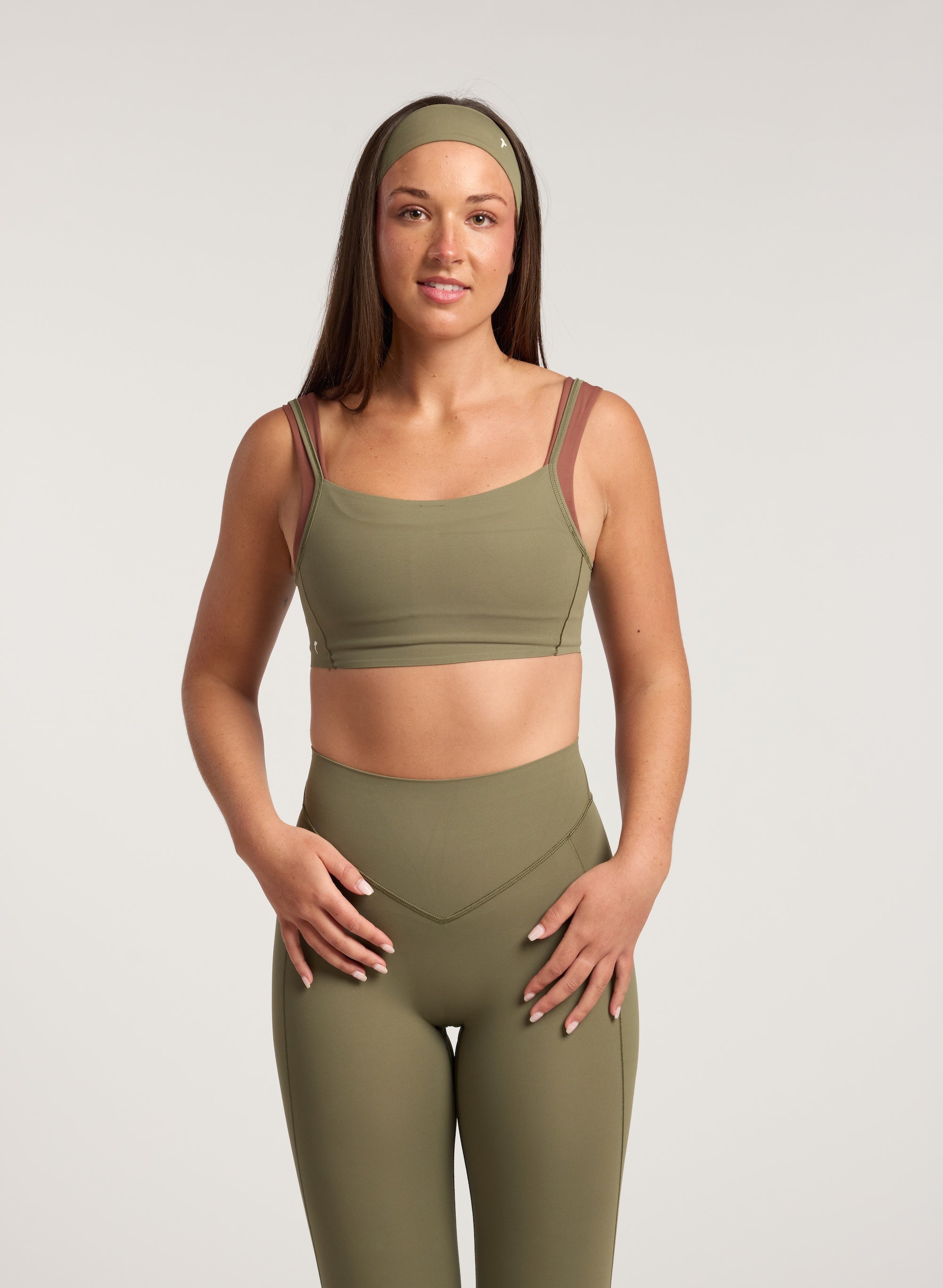 Woman wearing a green sports bra and leggings set on a light gray background