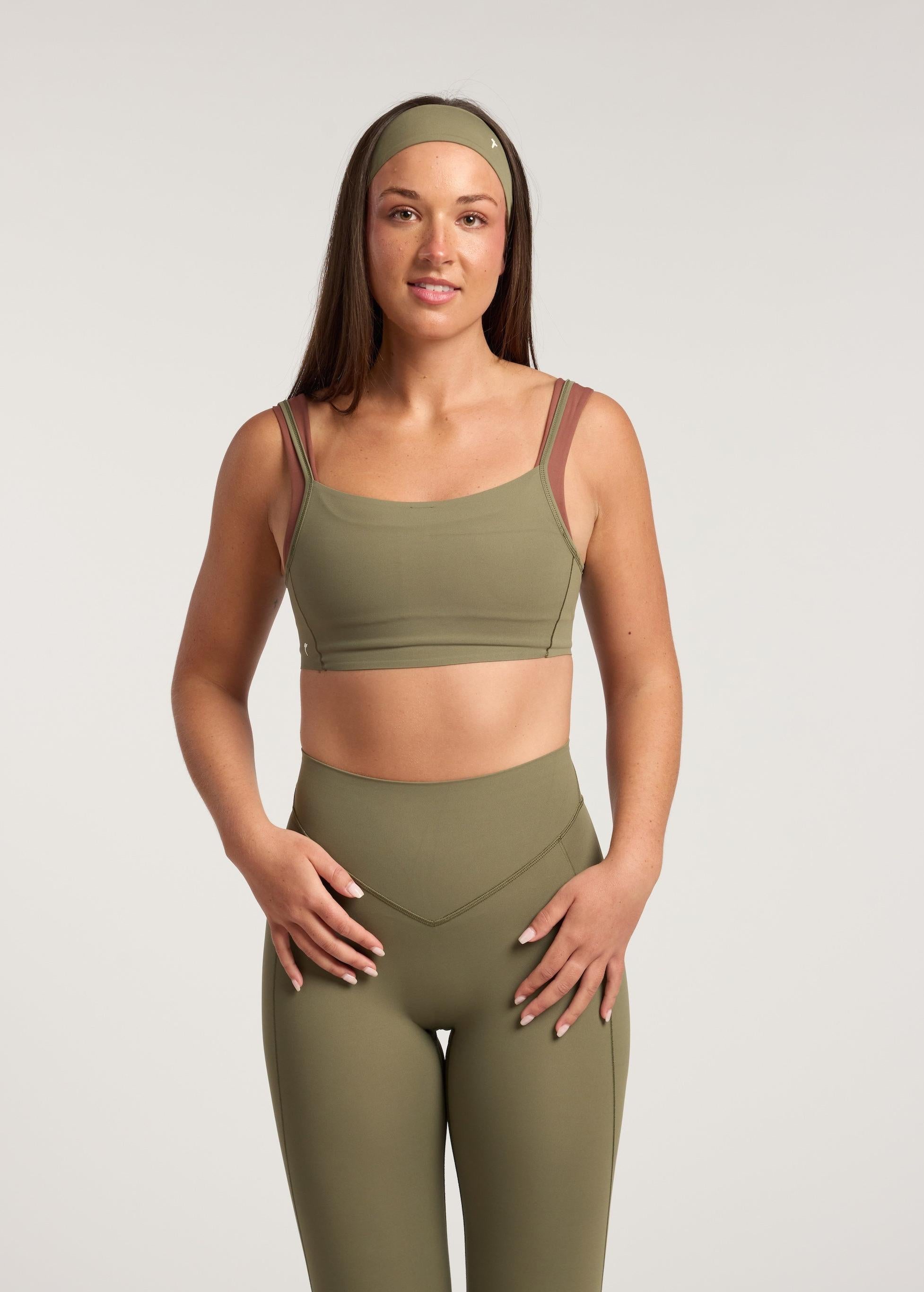 Woman wearing a green sports bra and leggings set on a light gray background