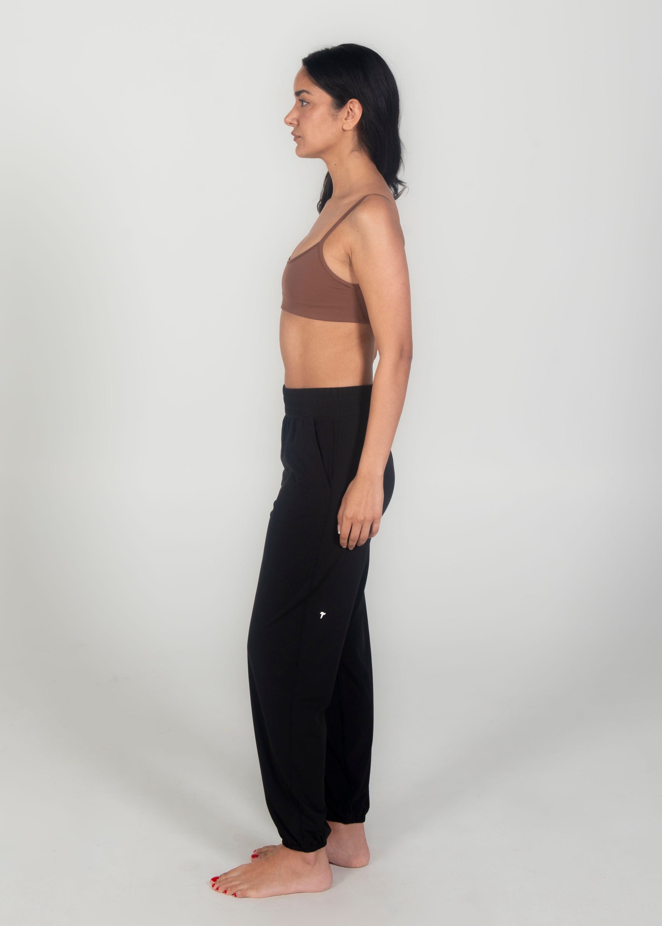 Woman wearing a brown sports bra and black pants on a white background