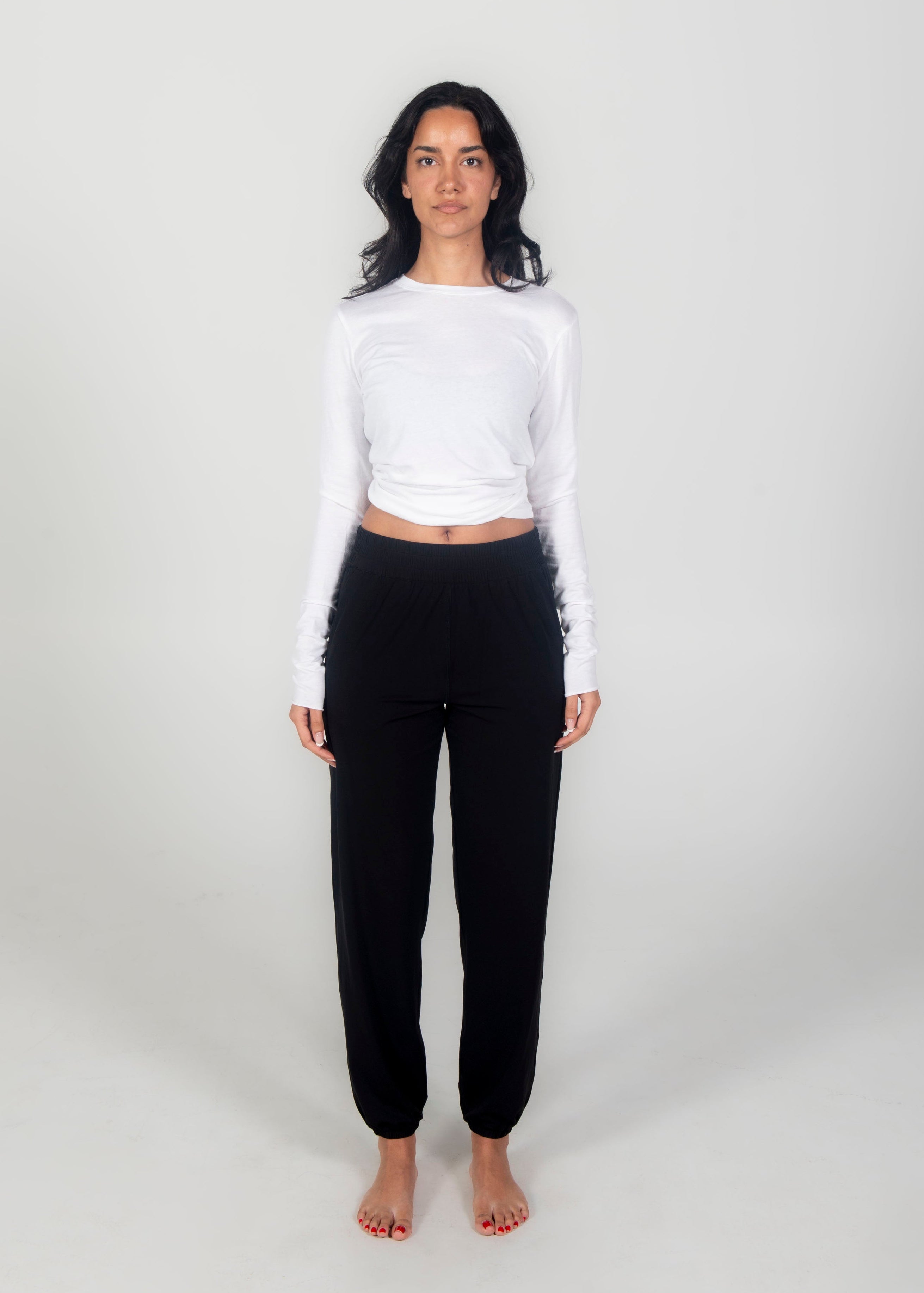 Person wearing a white long-sleeve top and black pants on a white background