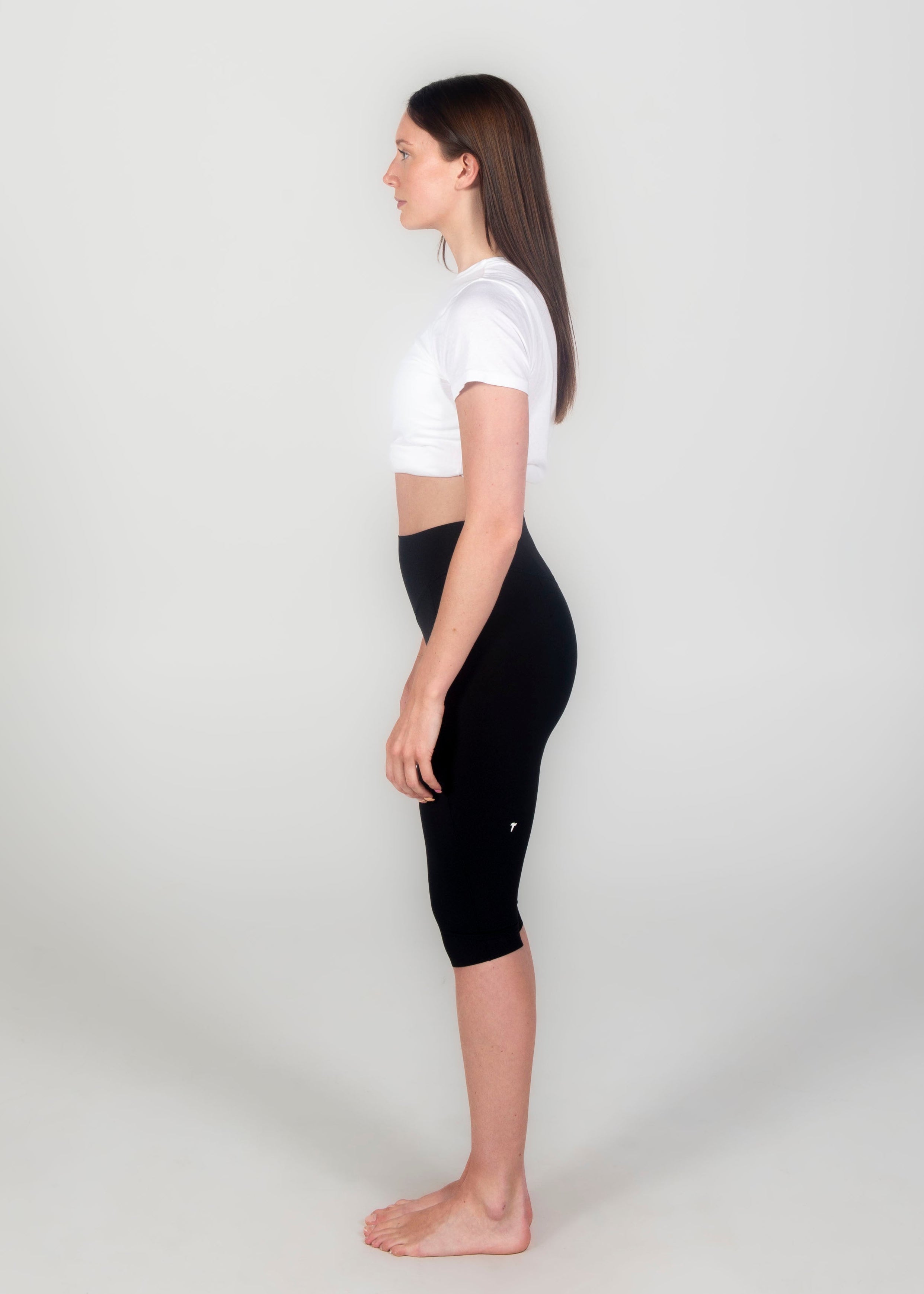 Woman wearing a white crop top and black capri leggings on a plain background