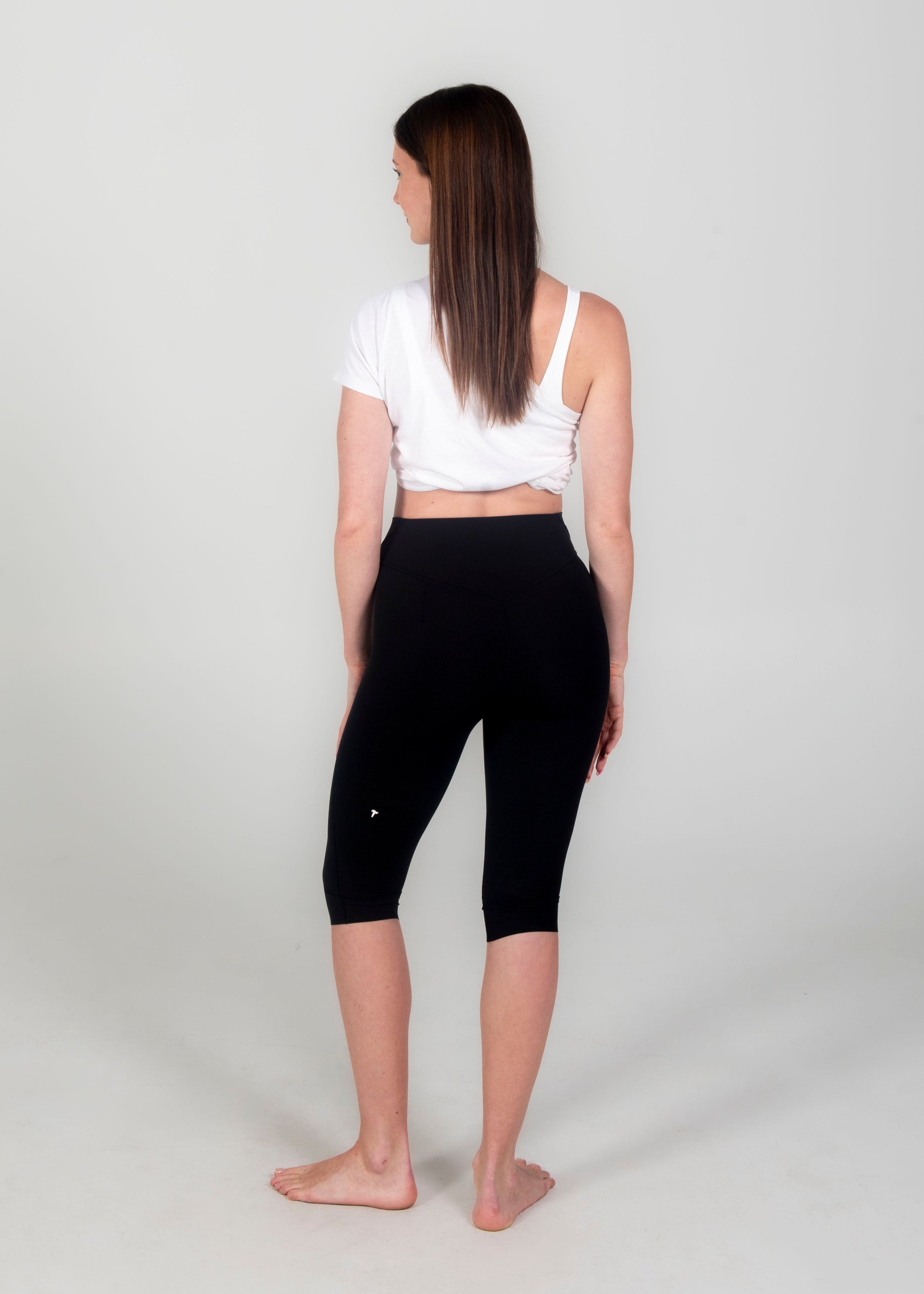 Woman wearing a white crop top and black capri leggings on a light gray background