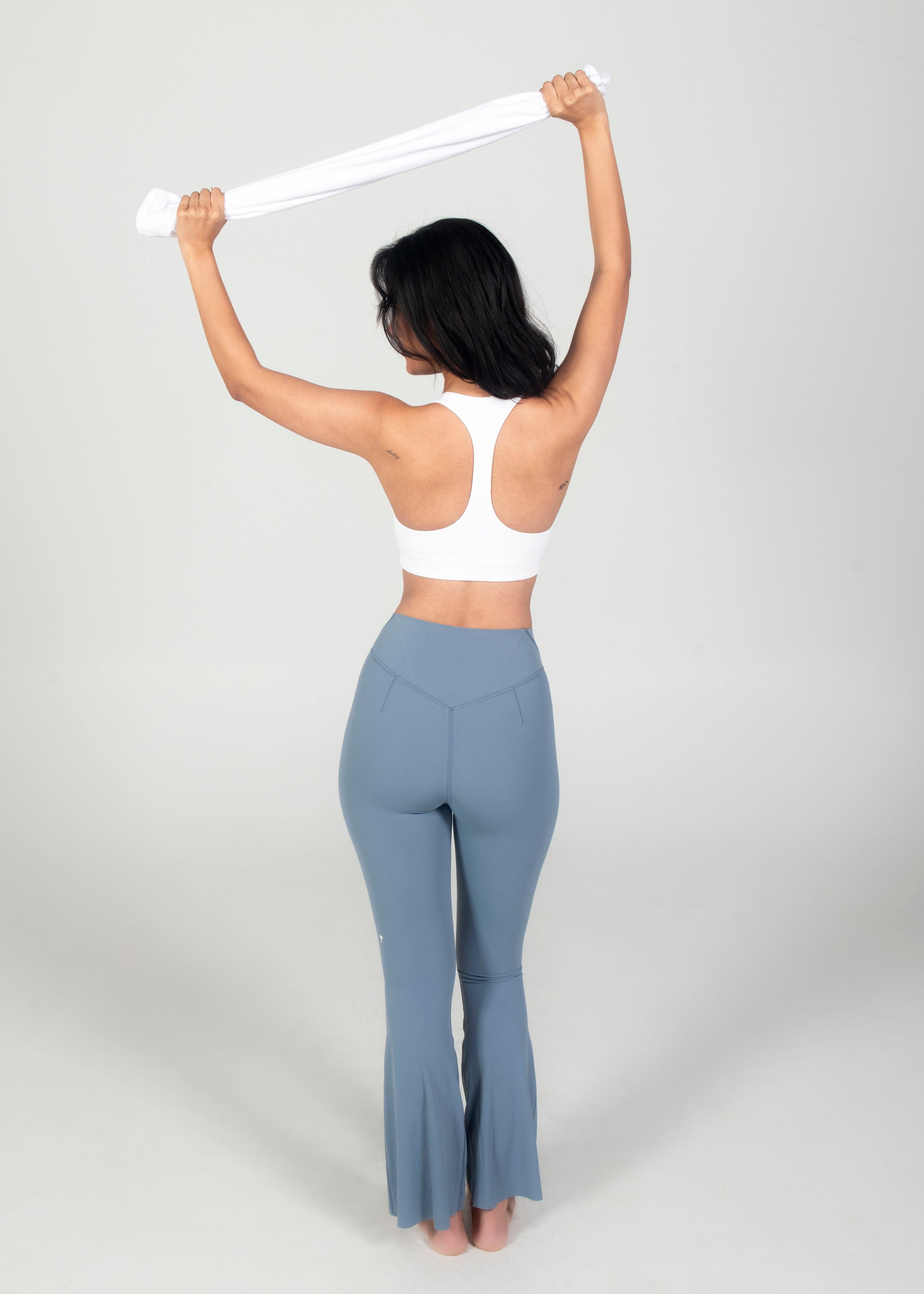 Person wearing a white sports bra and gray flared pants on a plain background