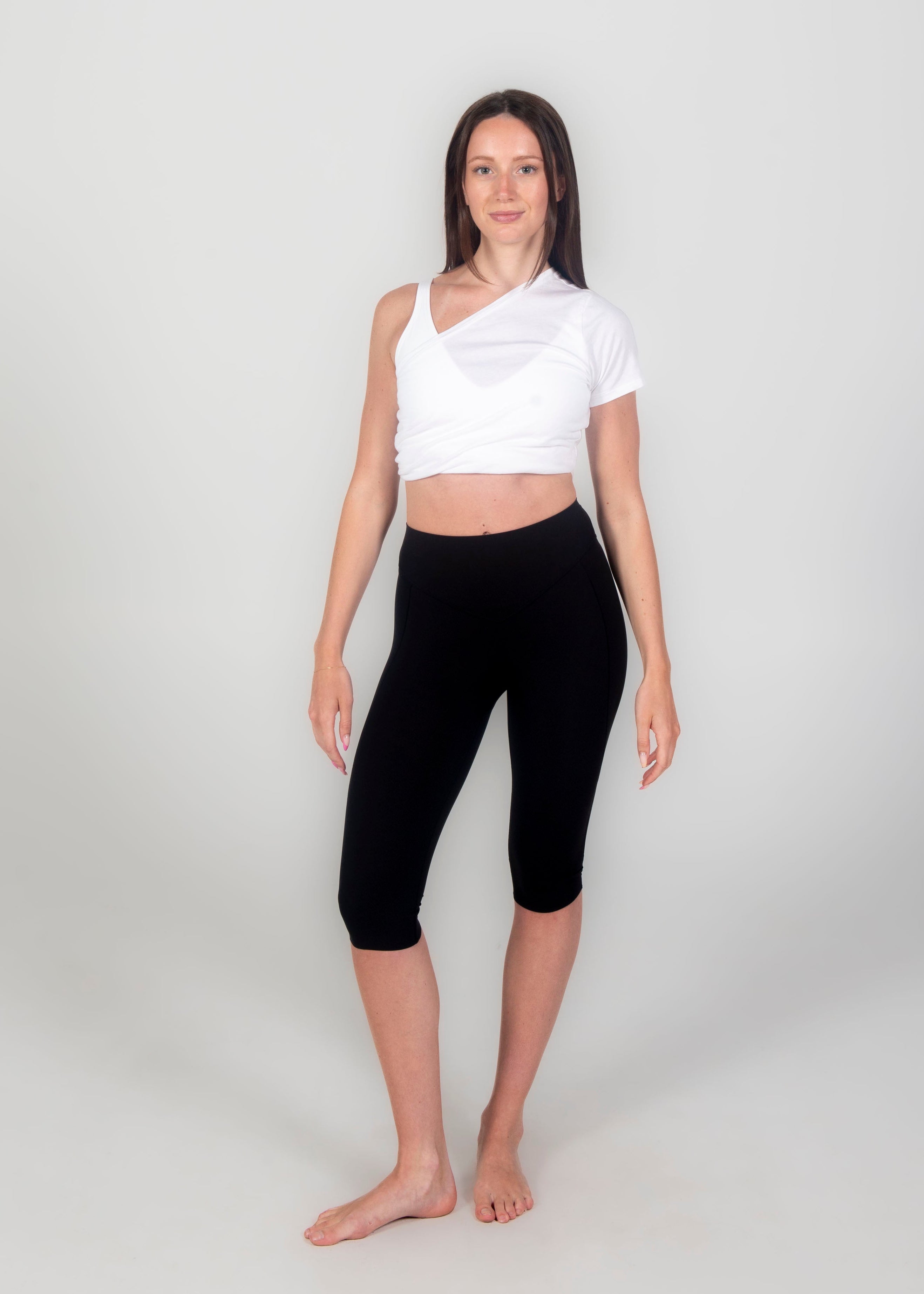 Woman wearing a white top and black capri leggings on a plain background