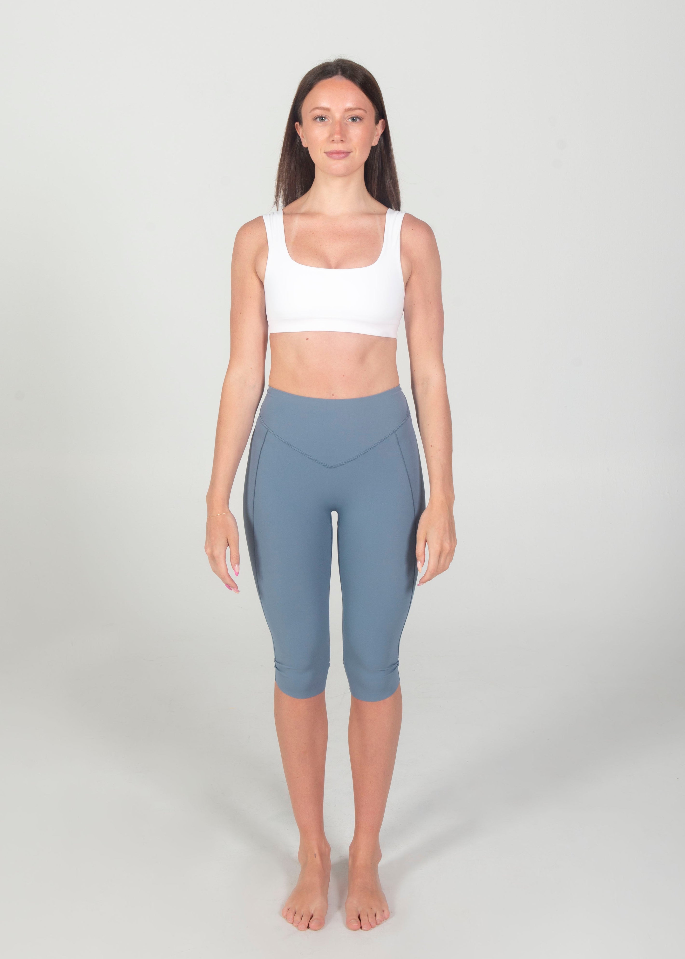 Woman wearing a white sports bra and gray leggings on a plain background