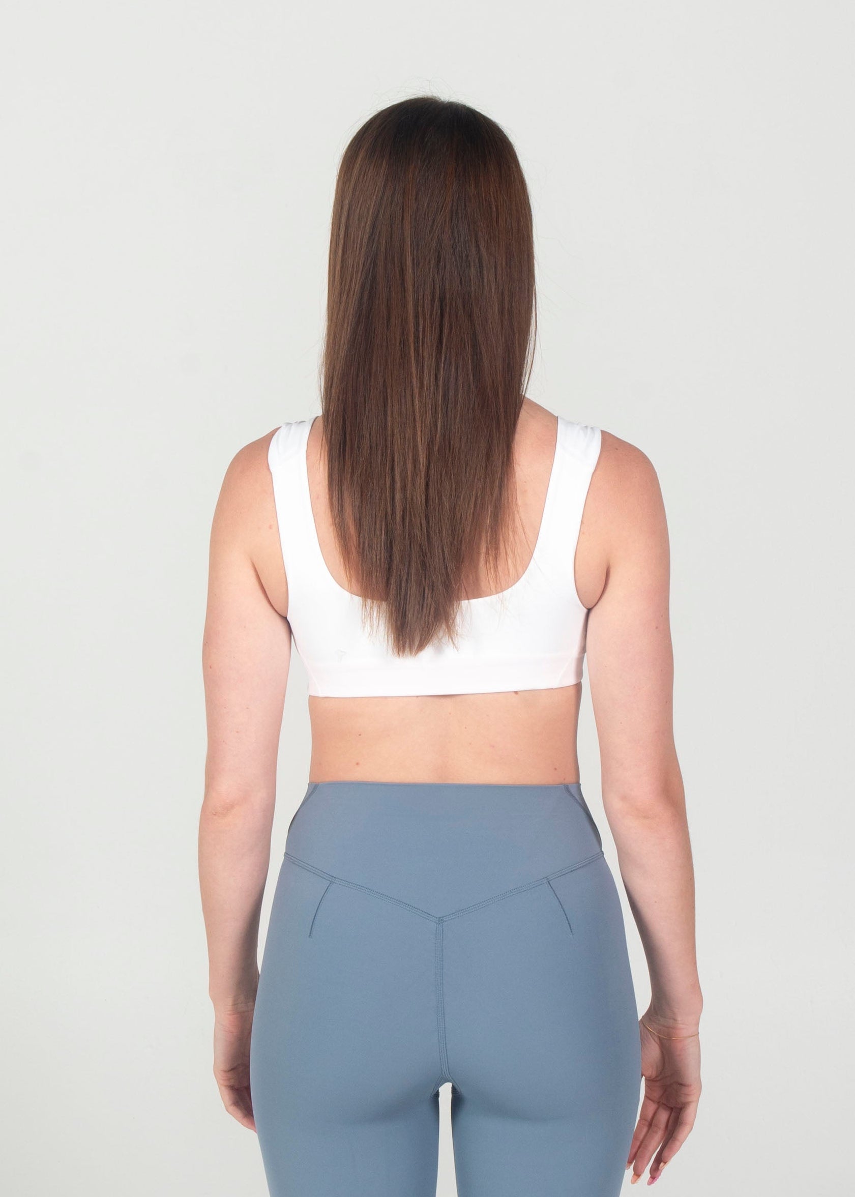 Person wearing a white sports bra and gray leggings on a white background
