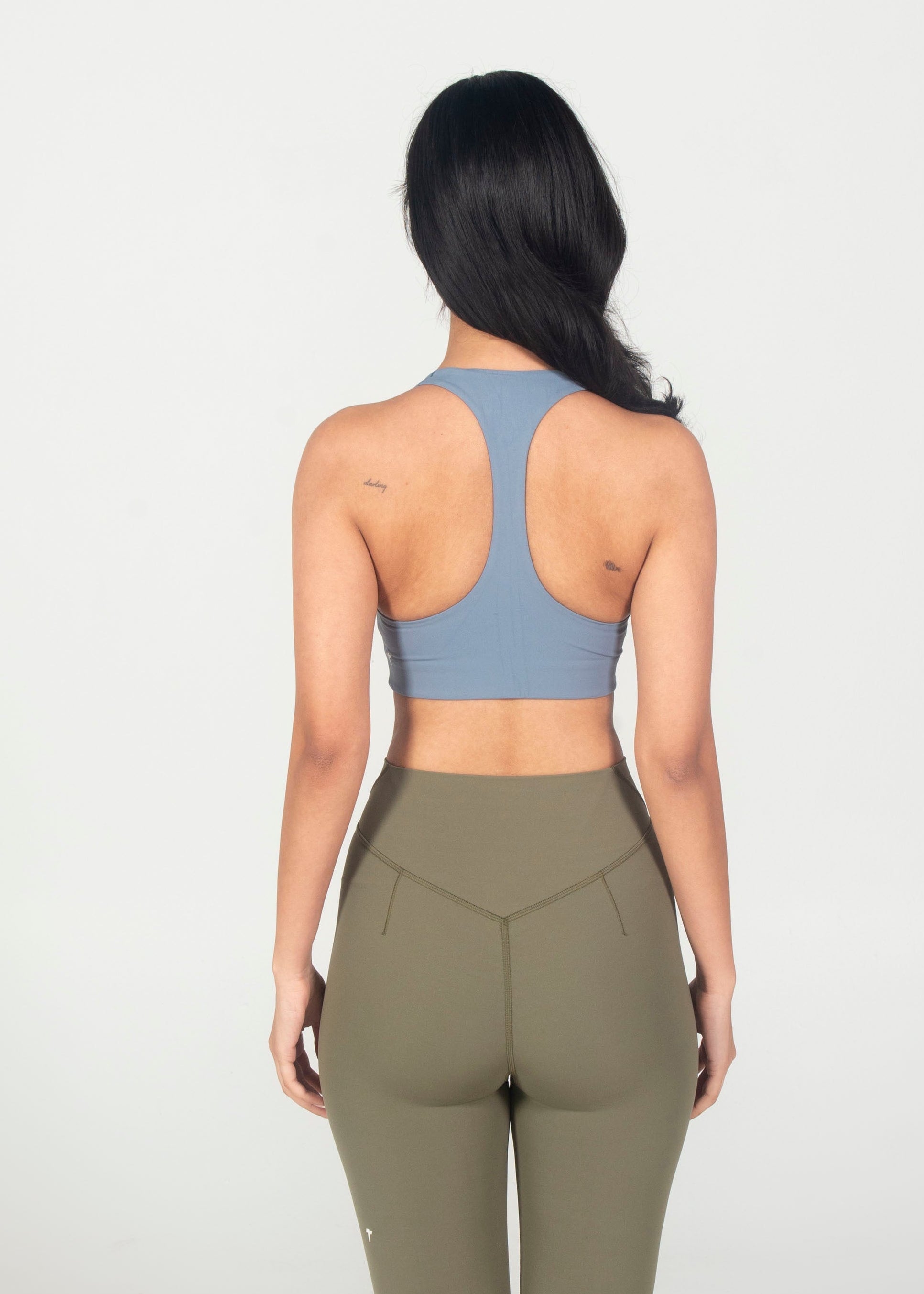 Woman wearing a blue sports bra and green leggings on a white background