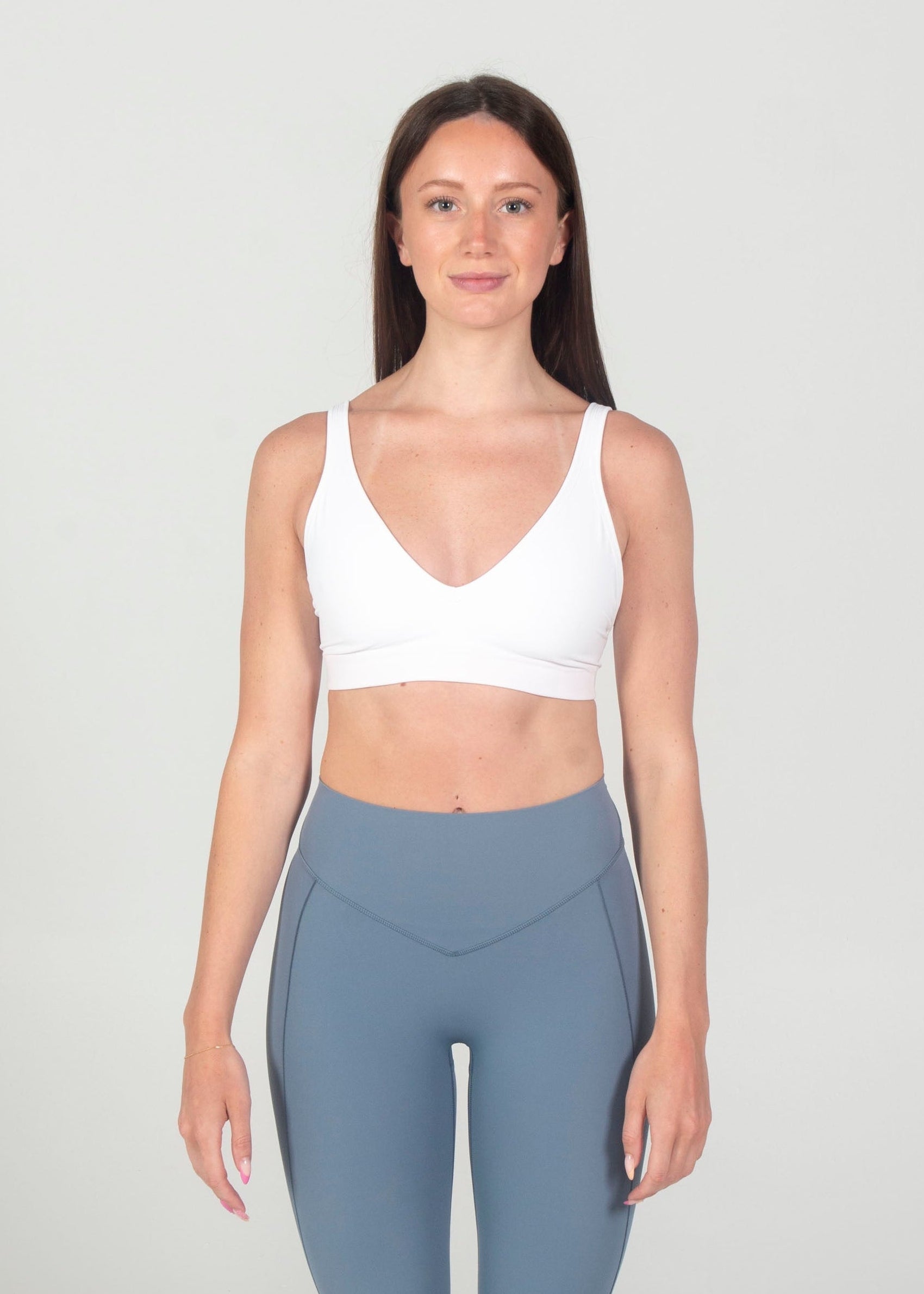 Woman wearing a white tank top and gray leggings on a plain background