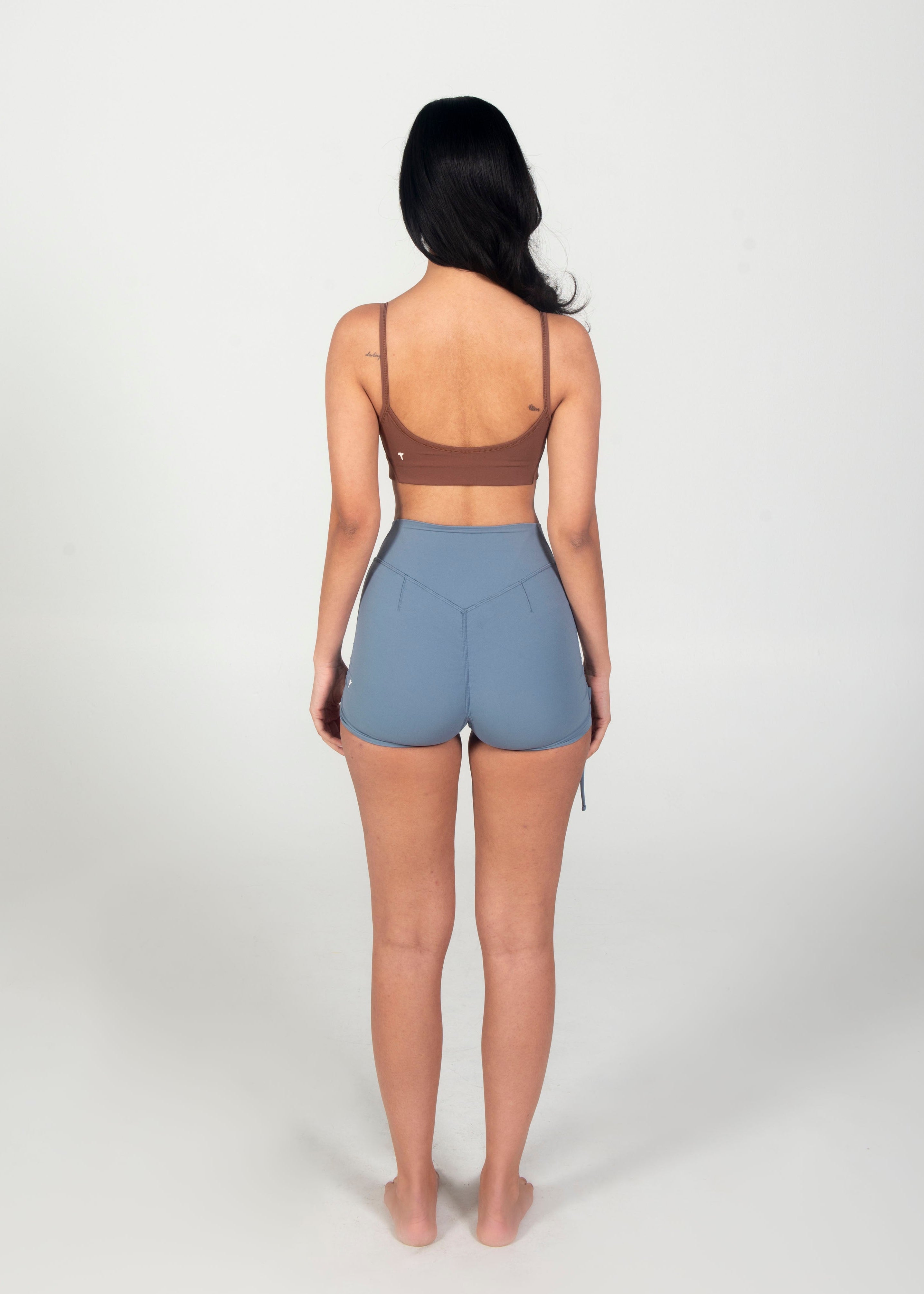 Woman wearing a brown sports bra and gray shorts on a white background