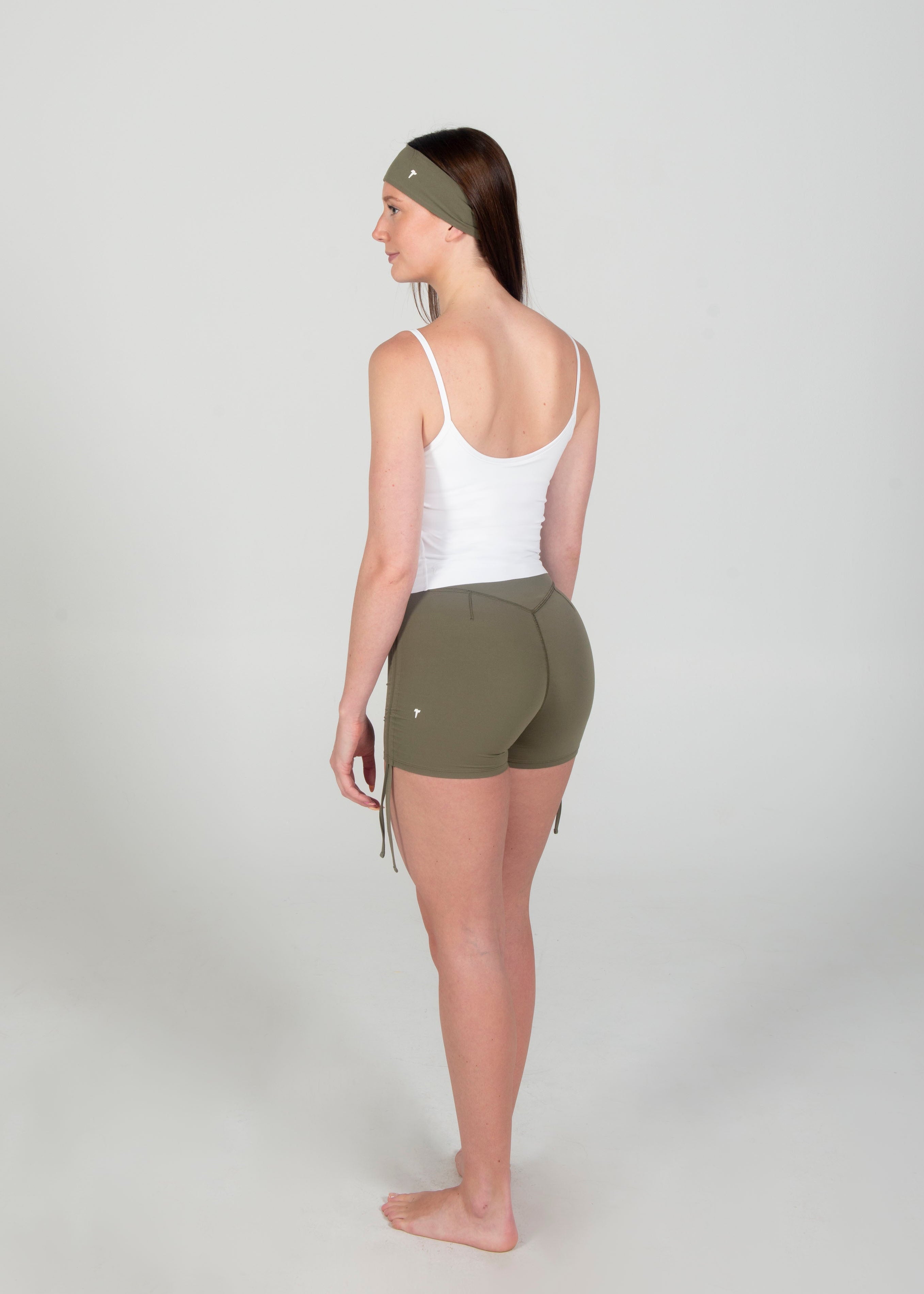 Woman wearing a white tank top and green shorts on a plain background
