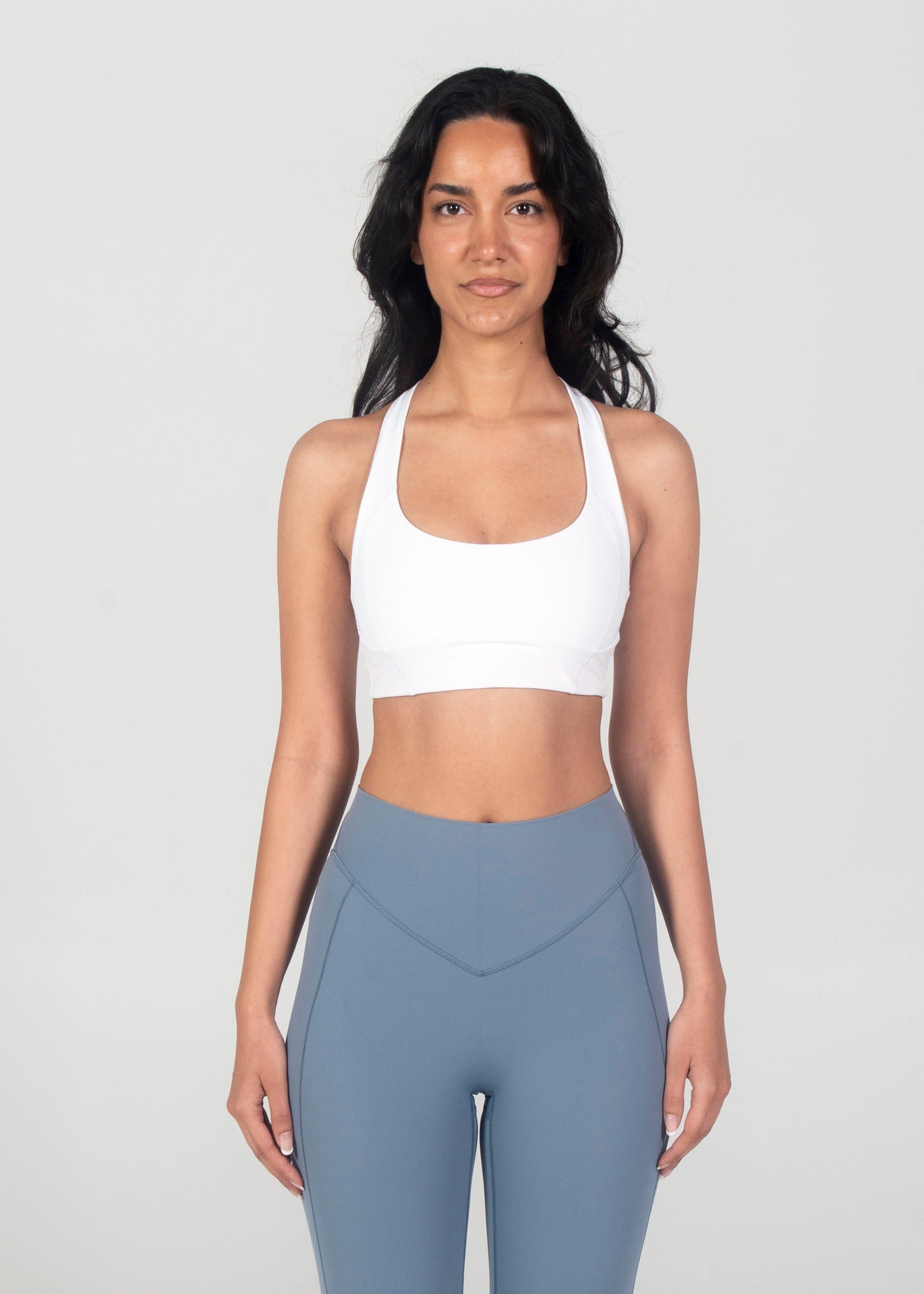 Woman wearing a white sports bra and gray leggings on a white background