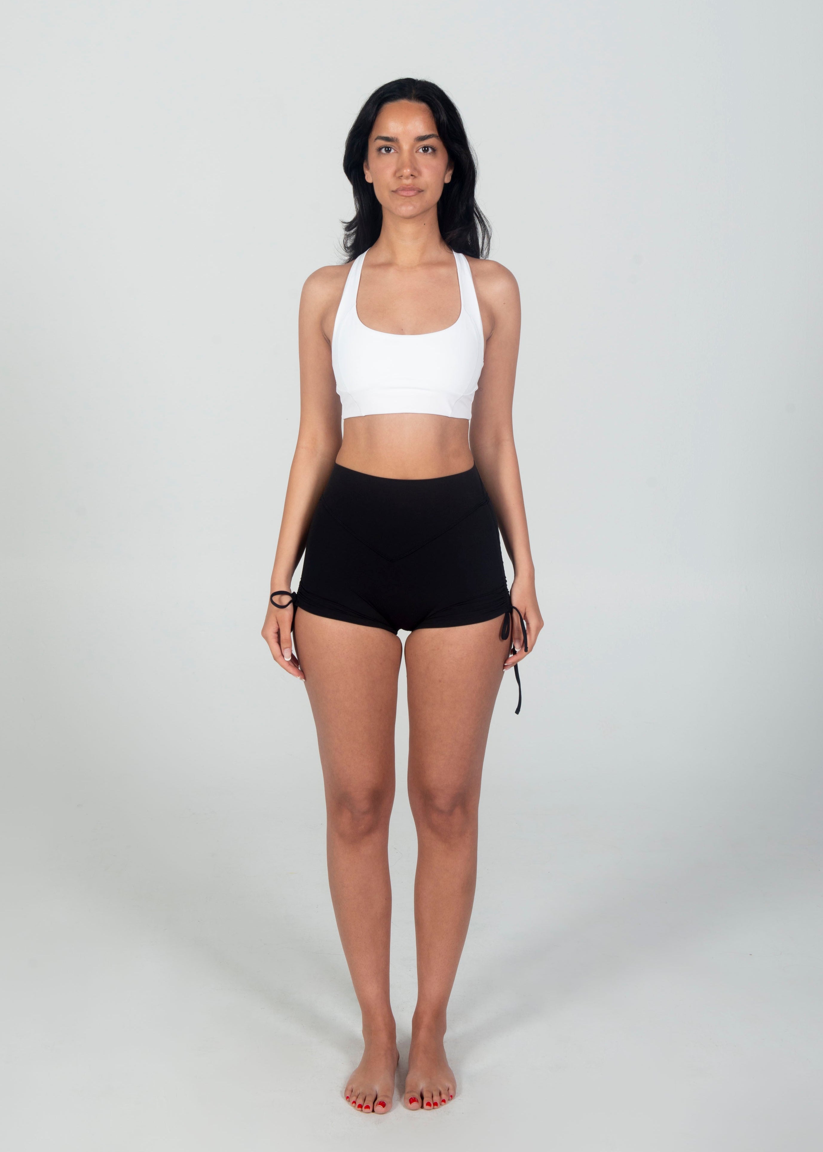 Woman wearing a white sports bra and black shorts on a plain background