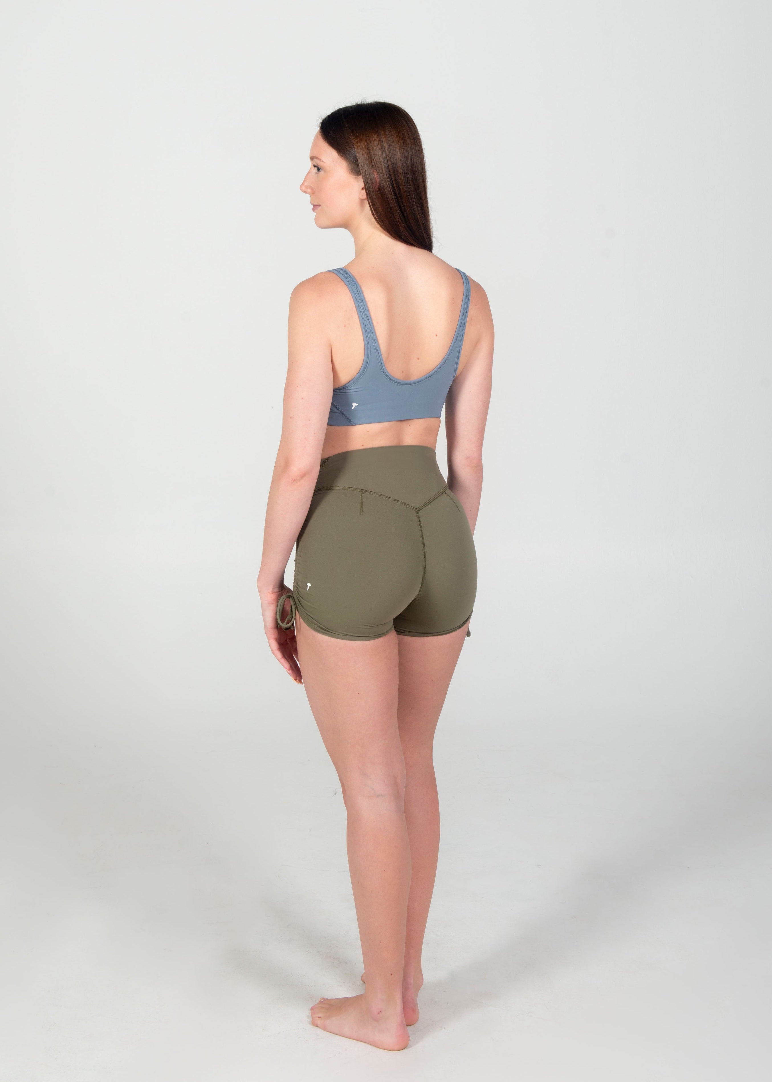 Woman wearing a blue sports bra and green shorts on a white background