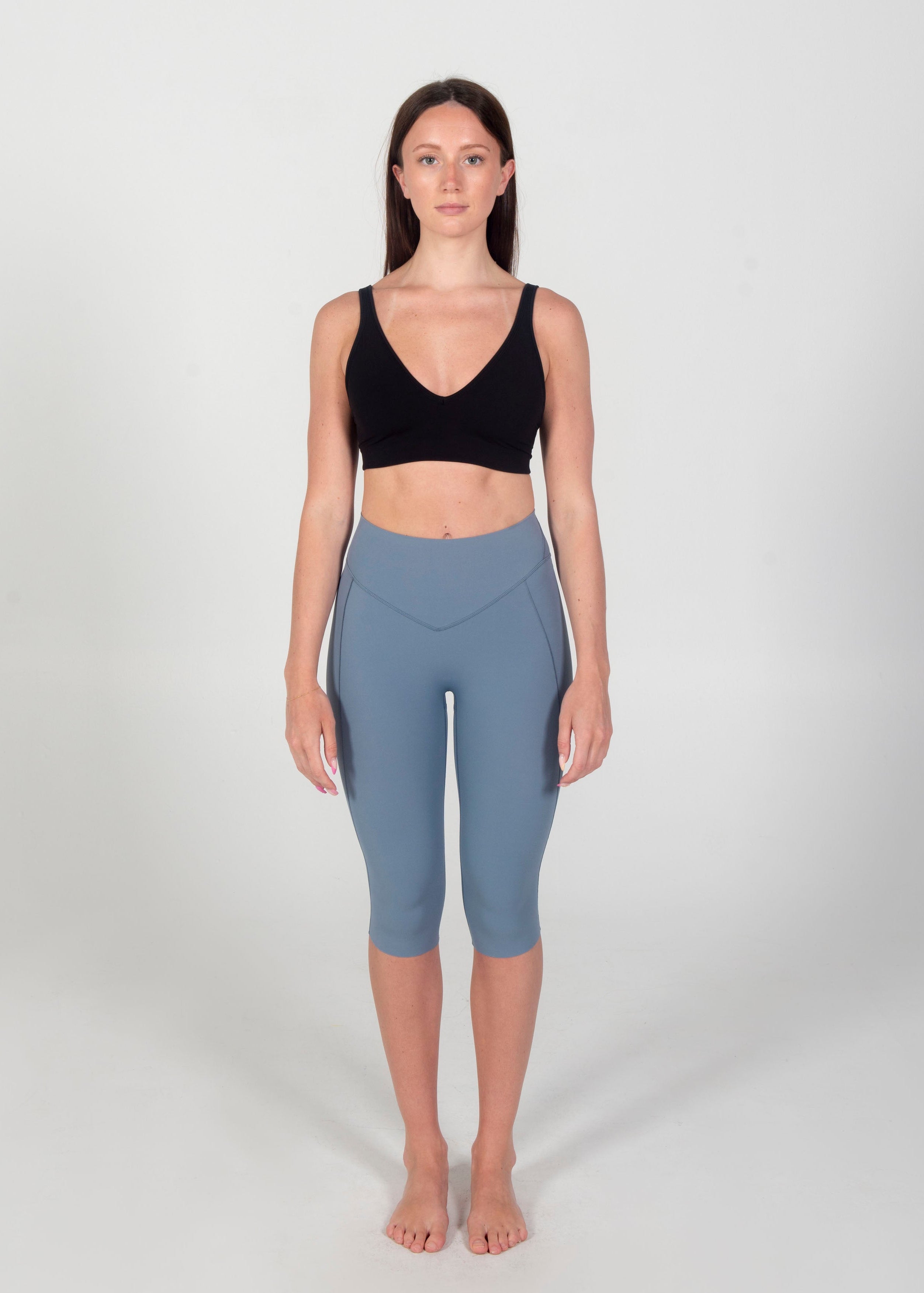 Woman wearing a black sports bra and light blue leggings on a white background