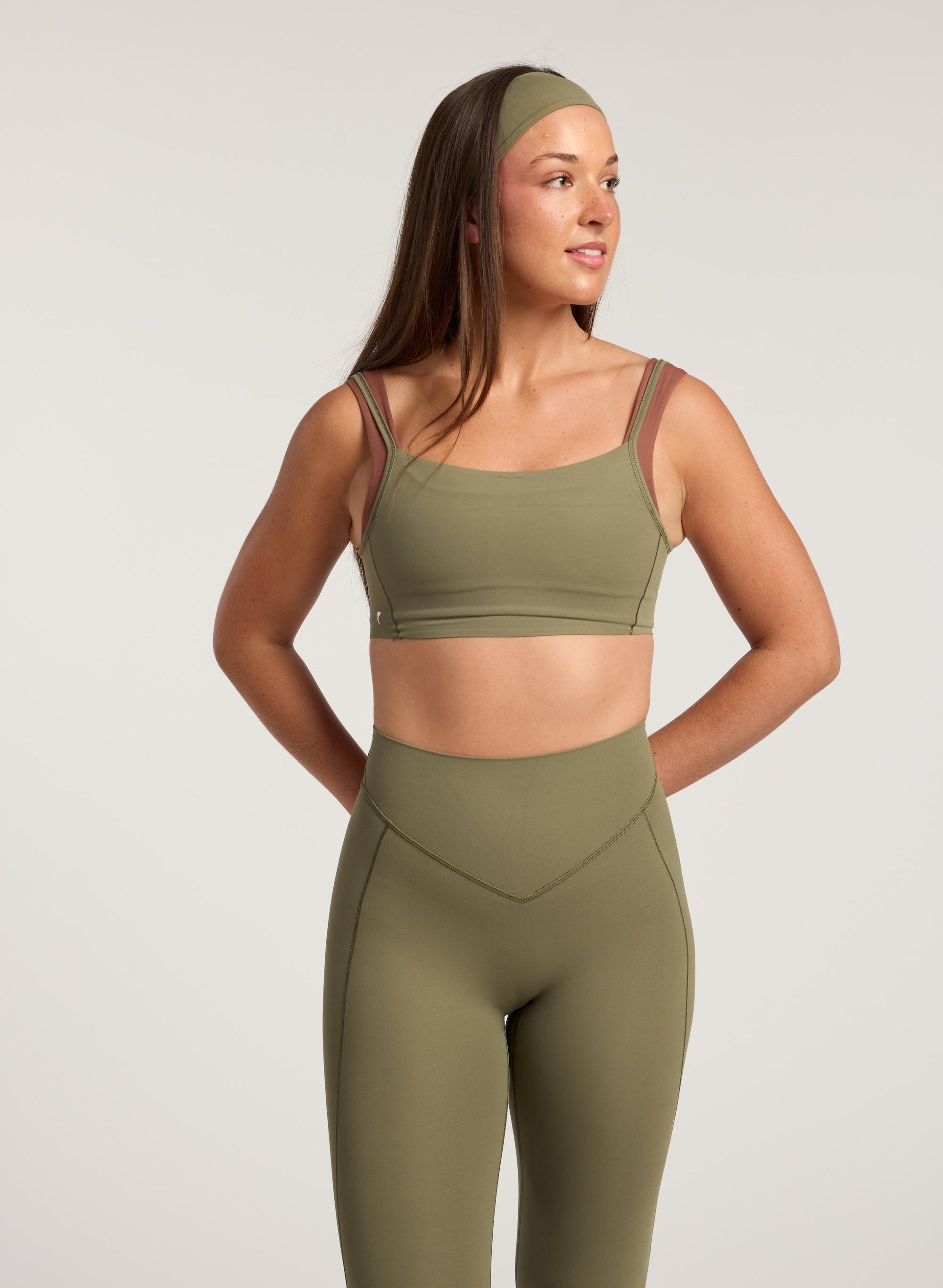 Woman wearing a green sports bra and leggings set on a light gray background