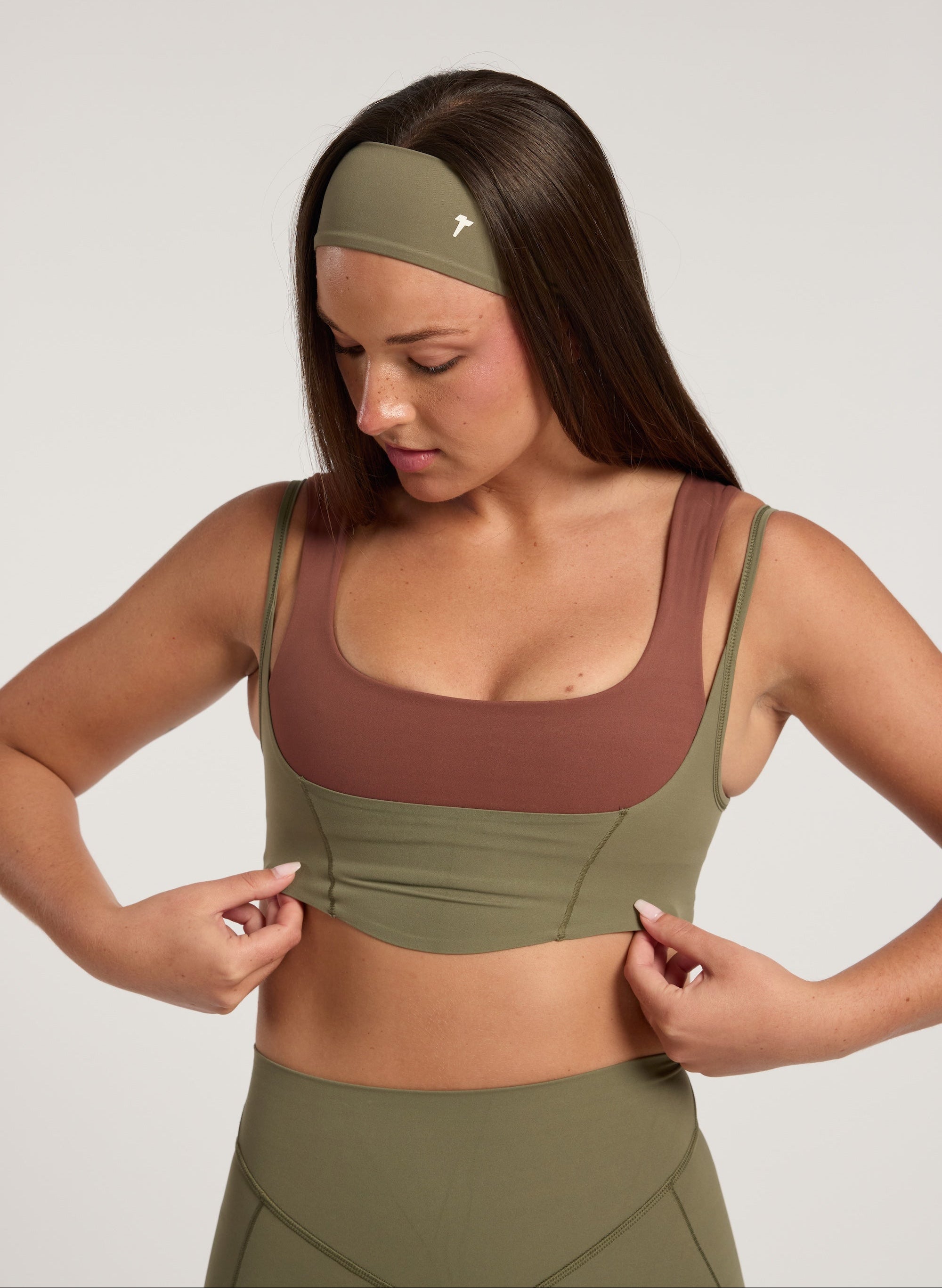 Woman wearing a green sports bra and leggings with a brown top on a white background