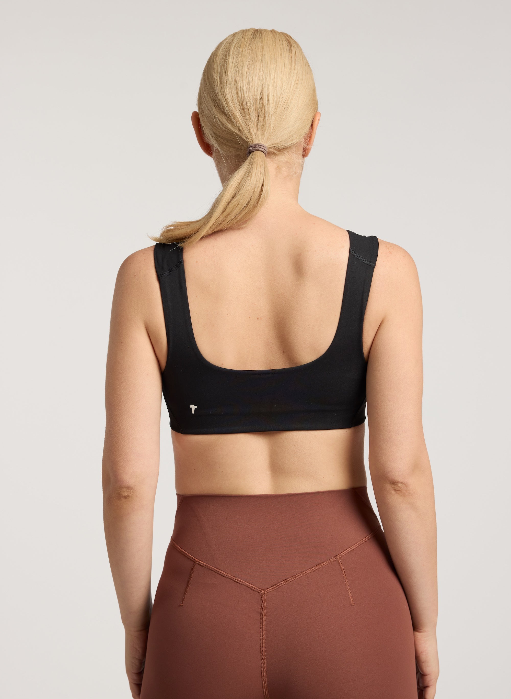 Person wearing a black sports bra and brown leggings on a plain background