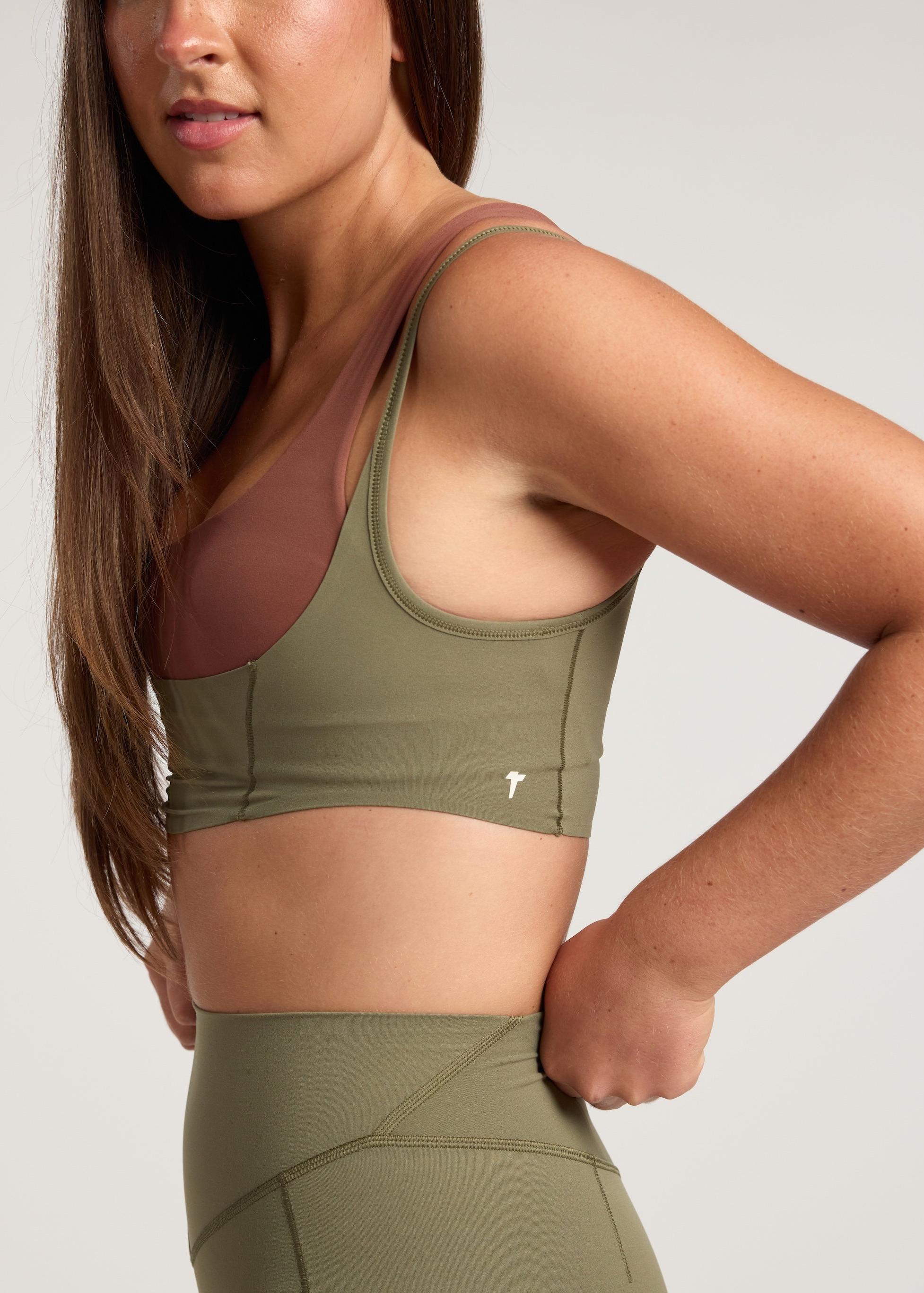Woman wearing an olive green sports bra and leggings on a light gray background