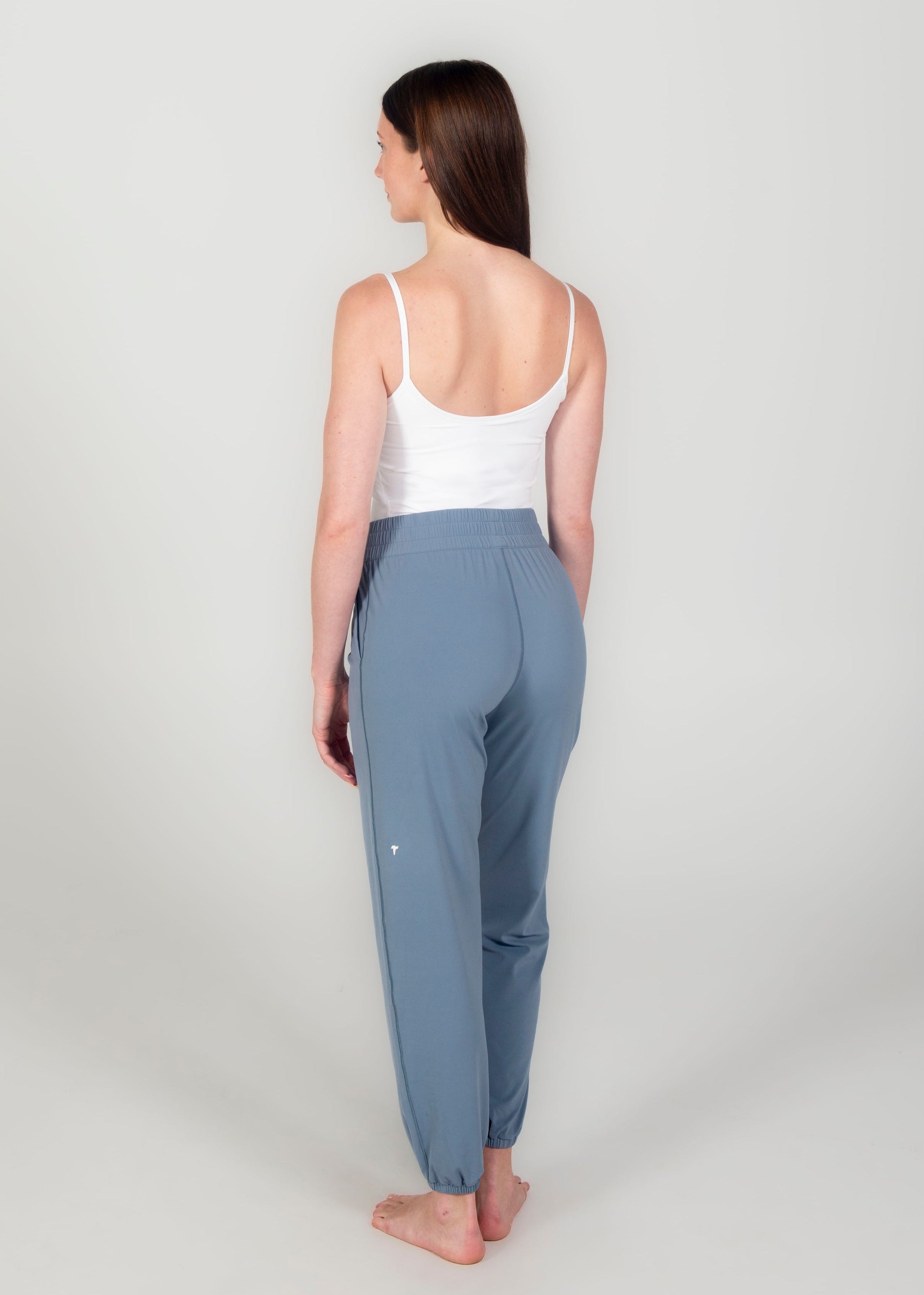 Woman wearing a white tank top and gray pants on a light gray background