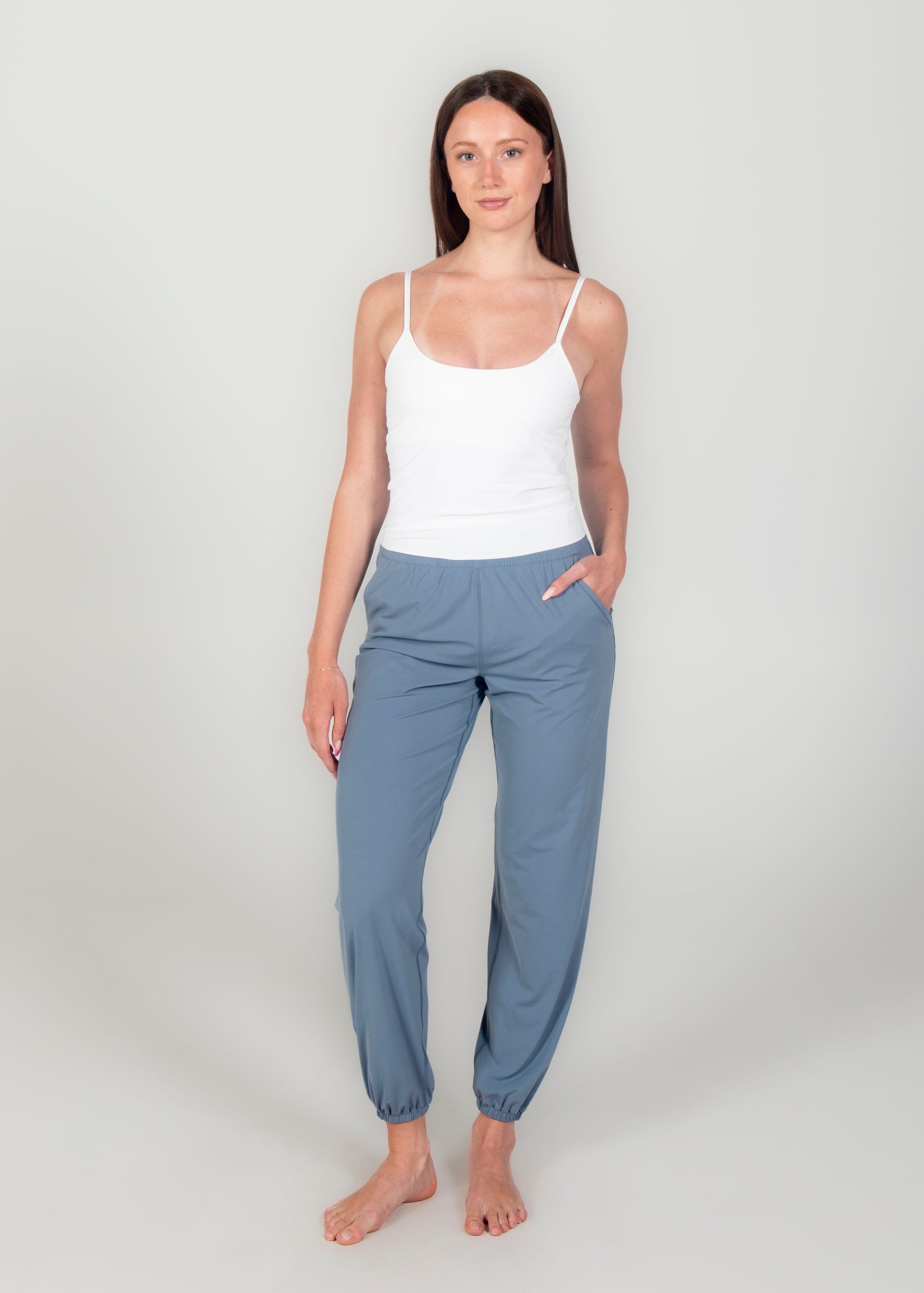 Woman wearing a white tank top and blue pants on a plain background
