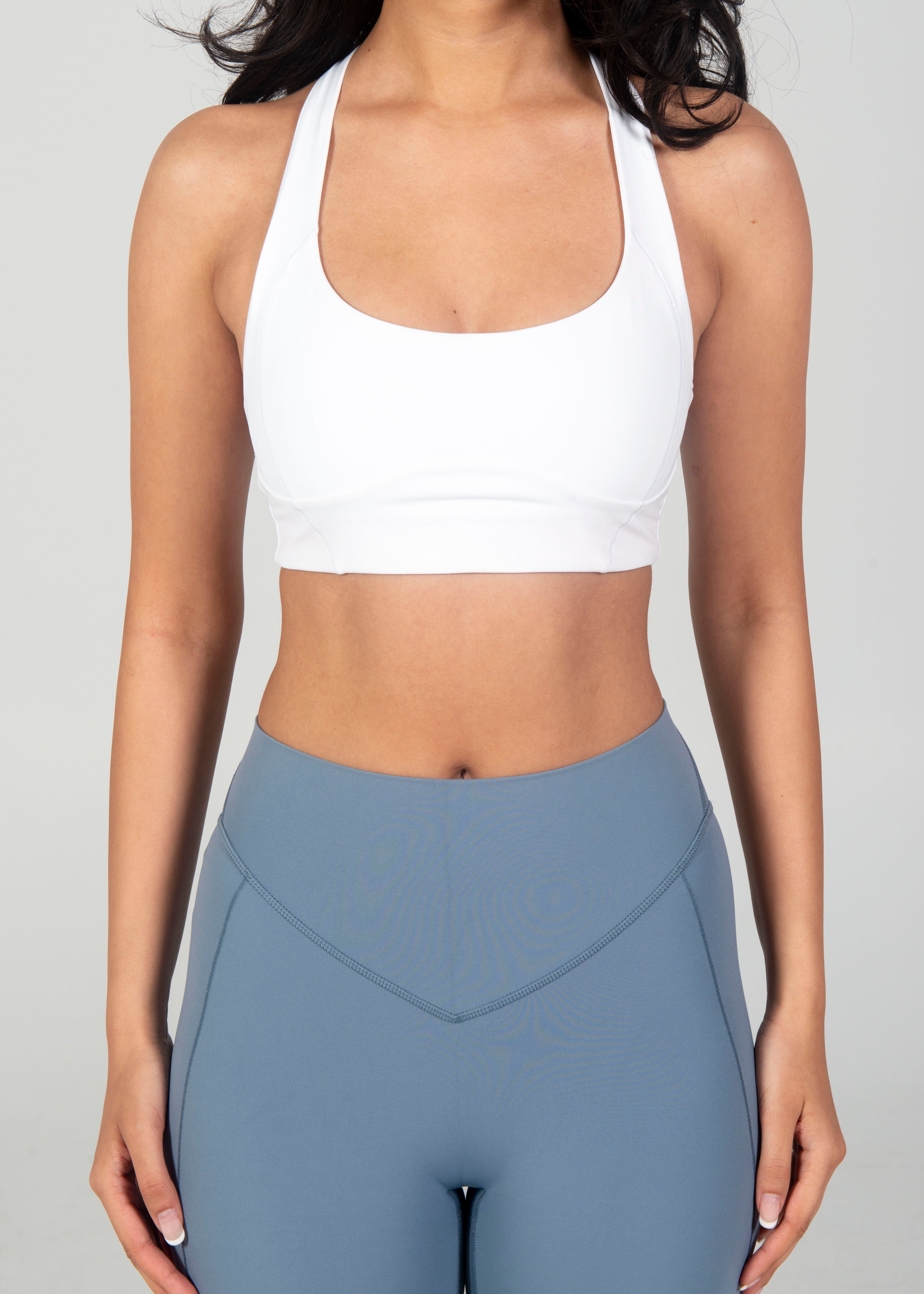 Person wearing a white sports bra and gray leggings on a plain background