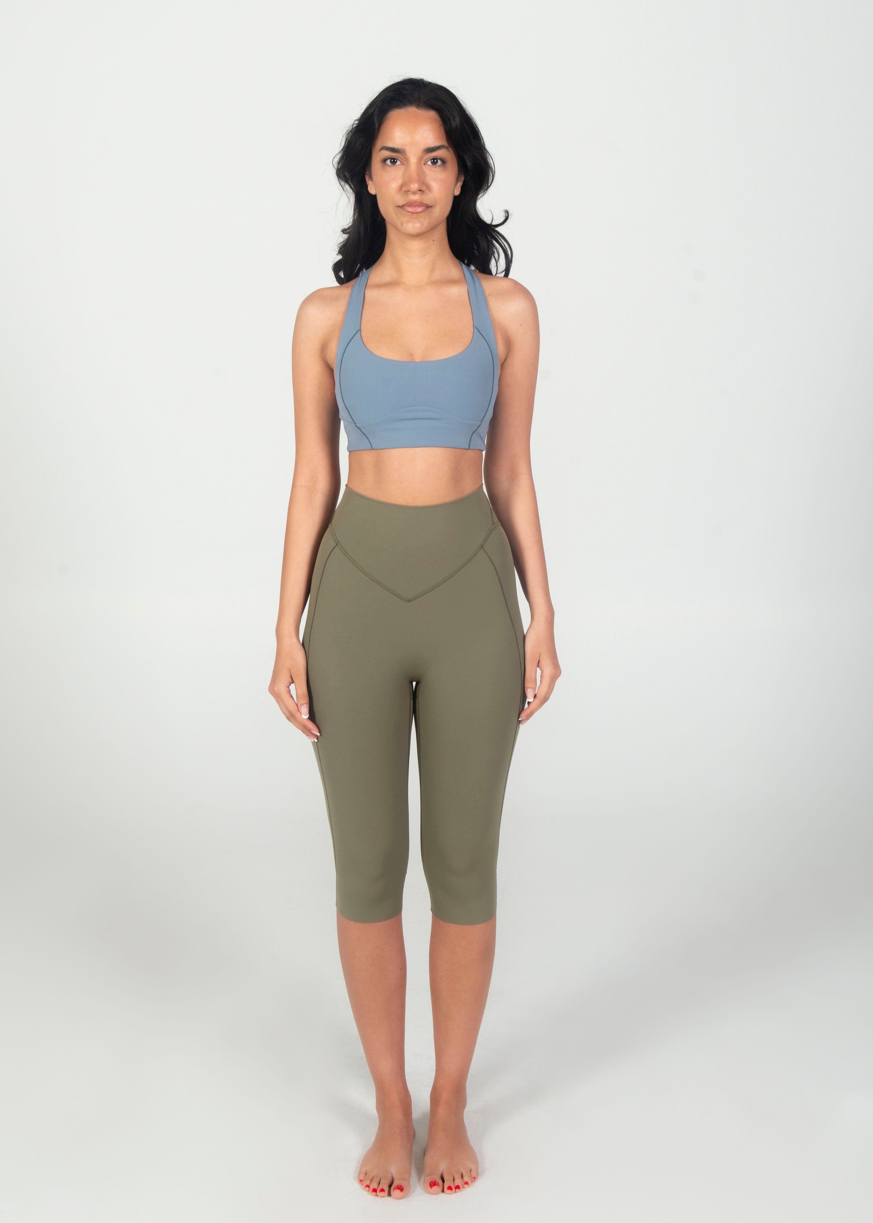 Woman wearing a blue sports bra and green leggings on a white background