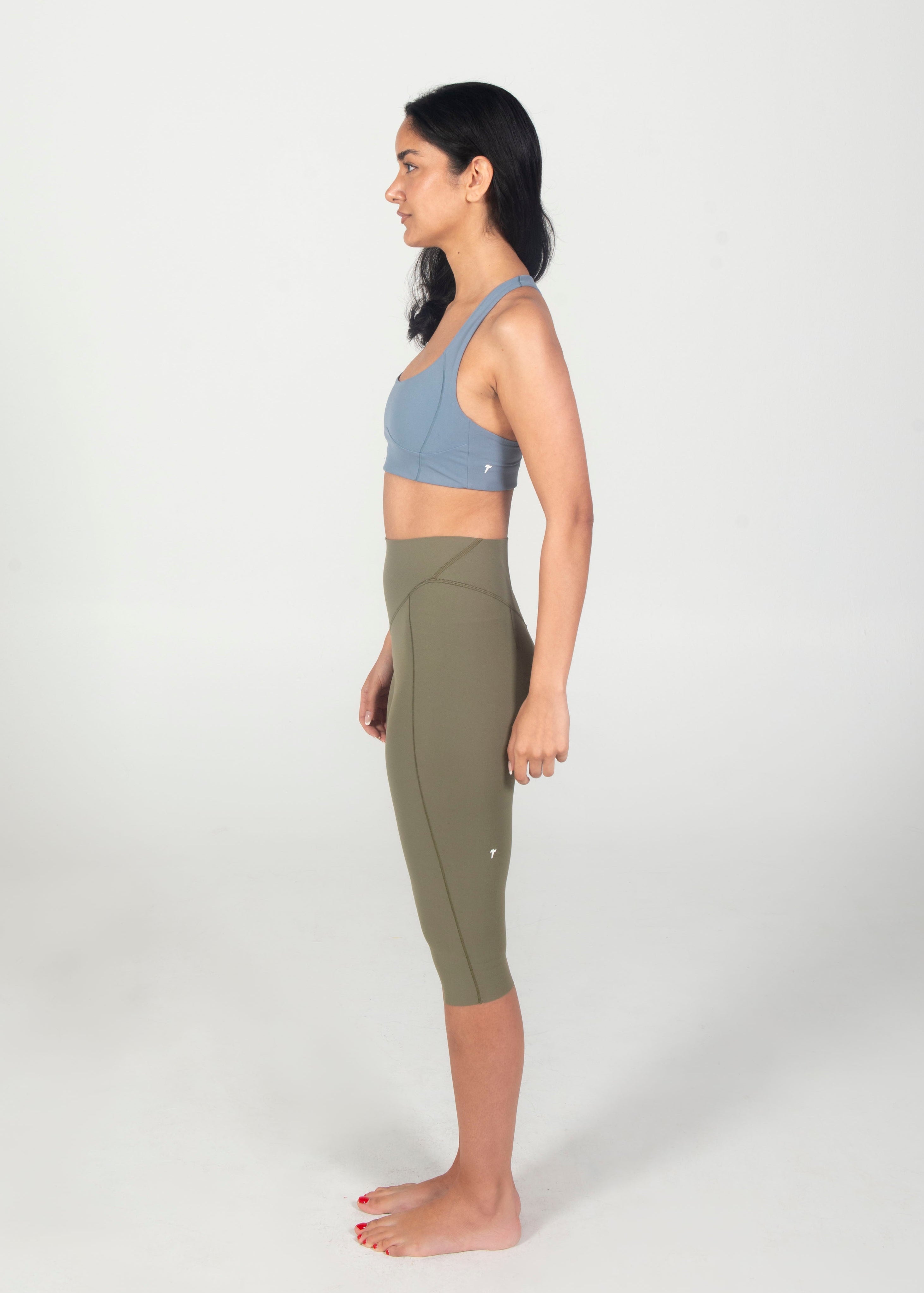 Woman wearing a blue sports bra and green leggings on a white background