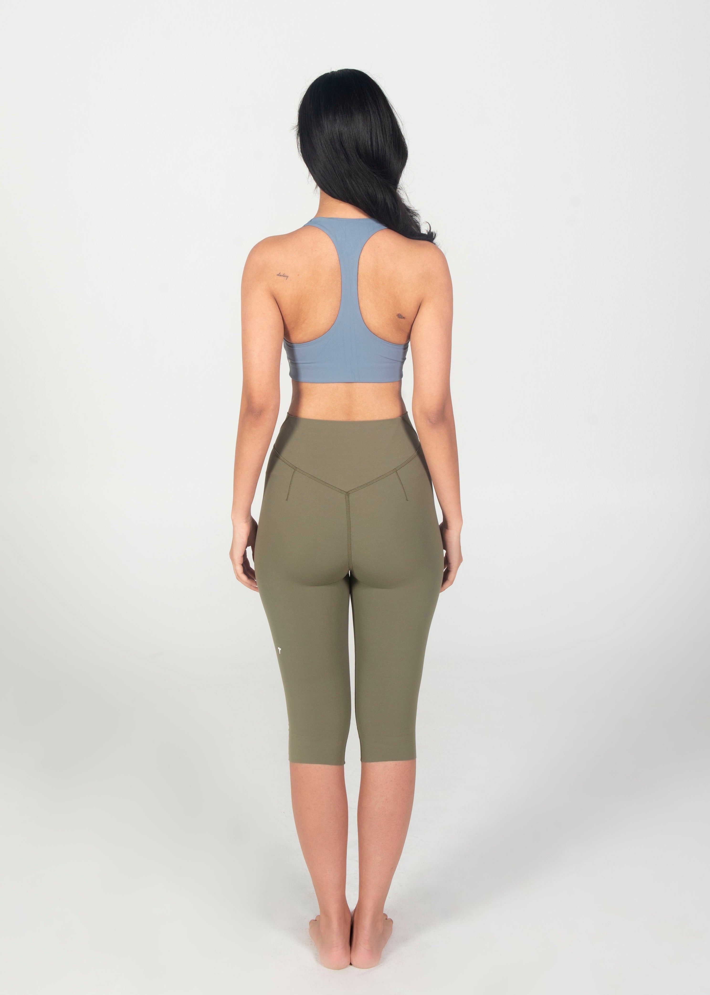 Woman wearing a blue sports bra and green leggings on a white background