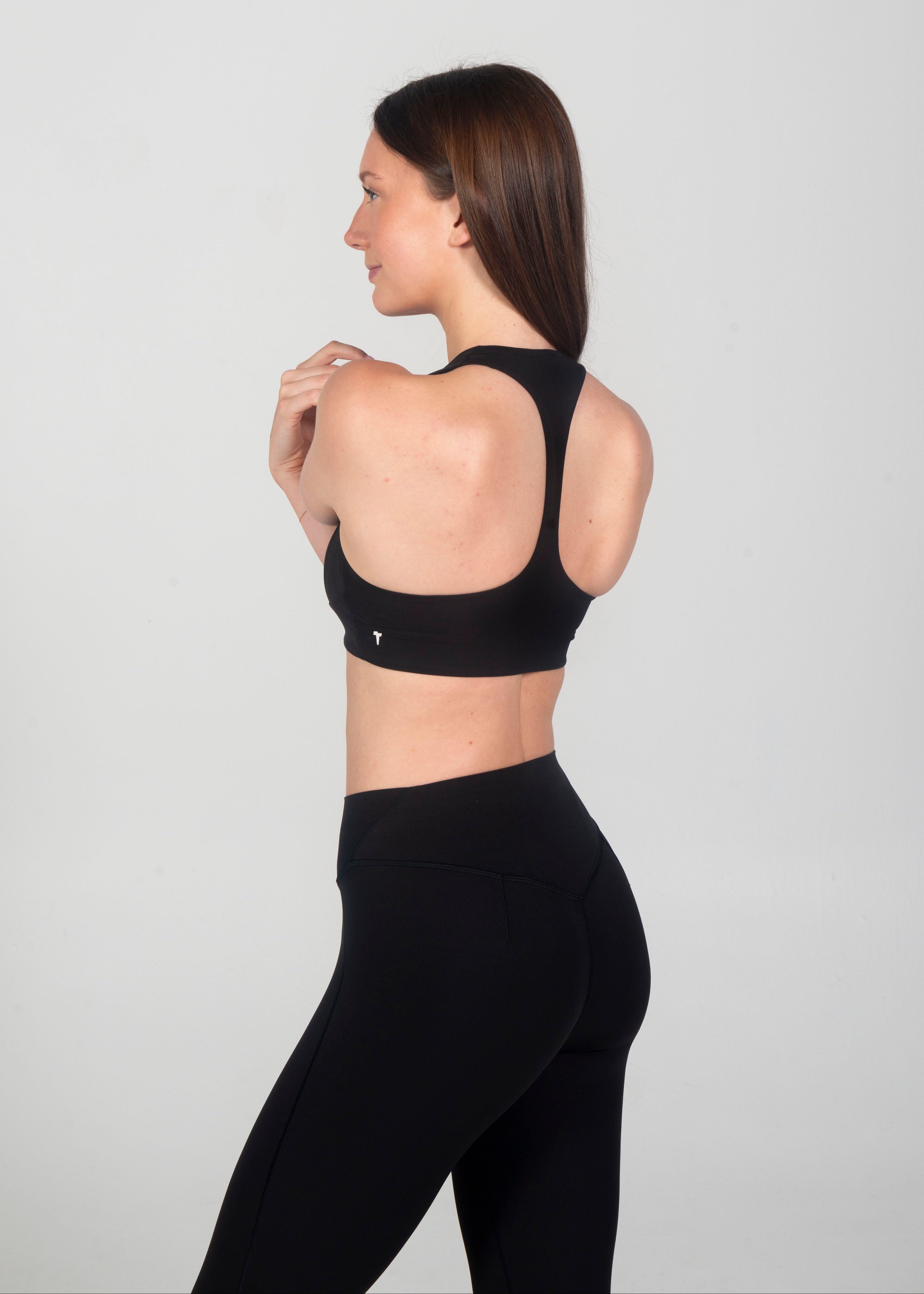 Woman wearing a black sports bra and leggings on a light gray background