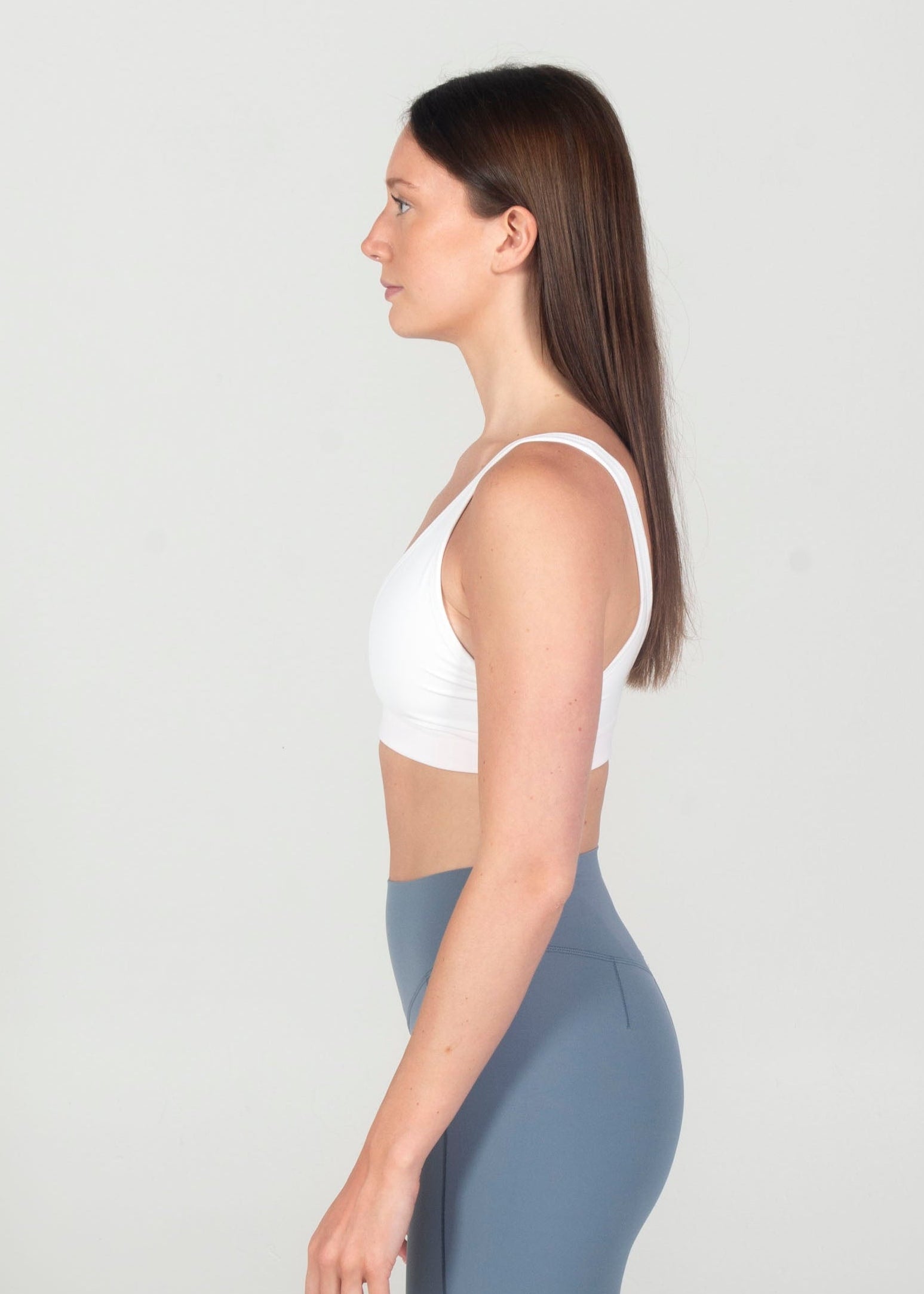 Woman wearing a white sports bra and blue capri leggings on a white background