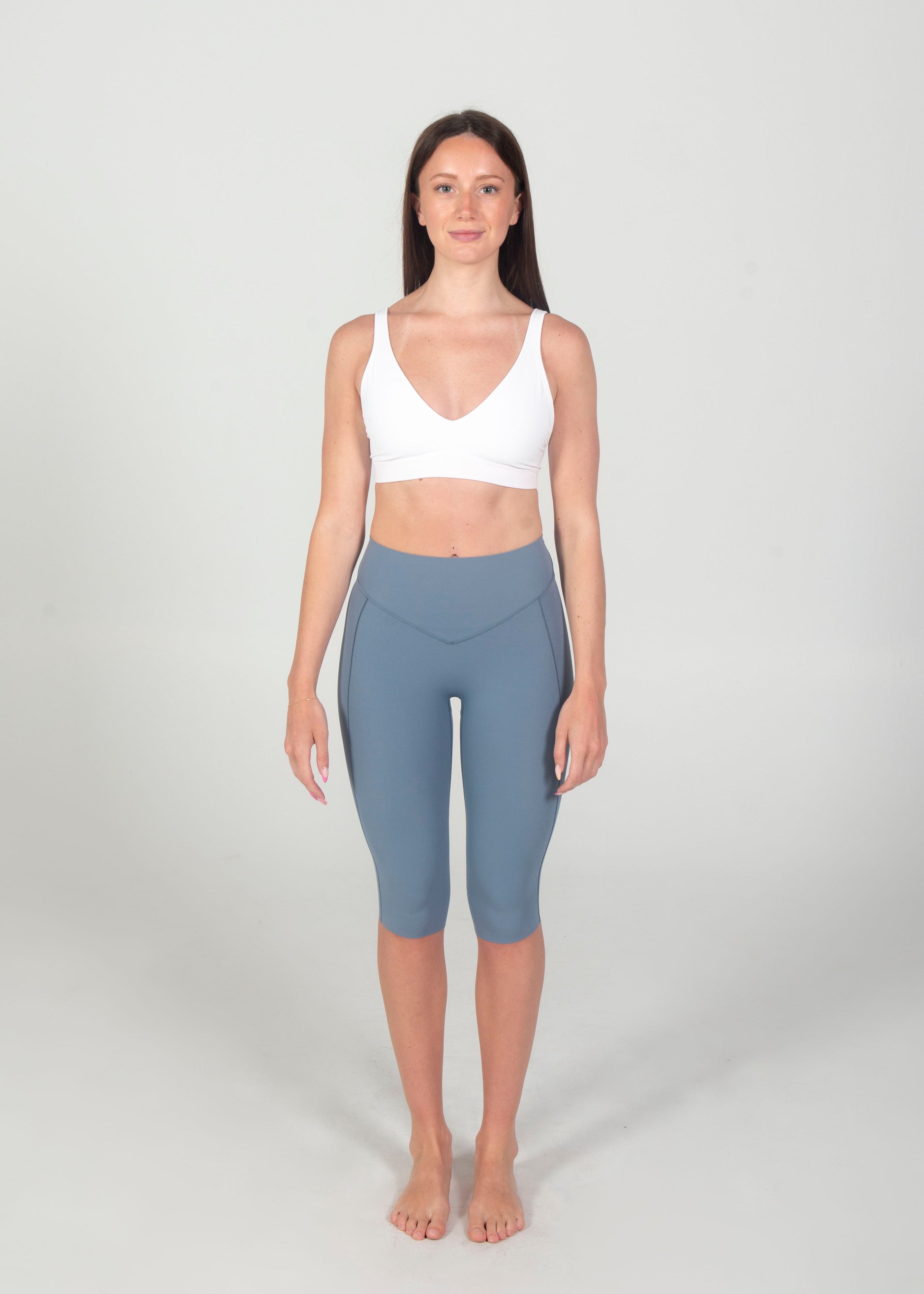 Woman wearing a white tank top and gray leggings on a plain background