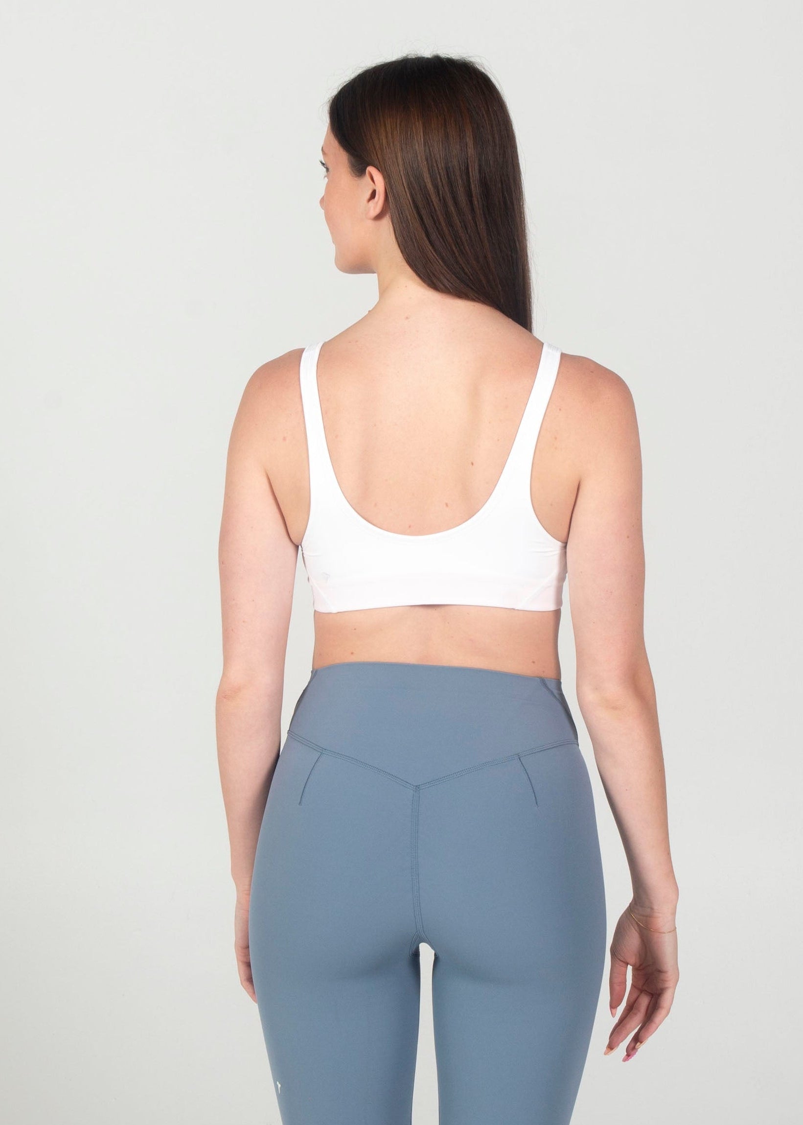 Person wearing a white sports bra and gray leggings on a white background