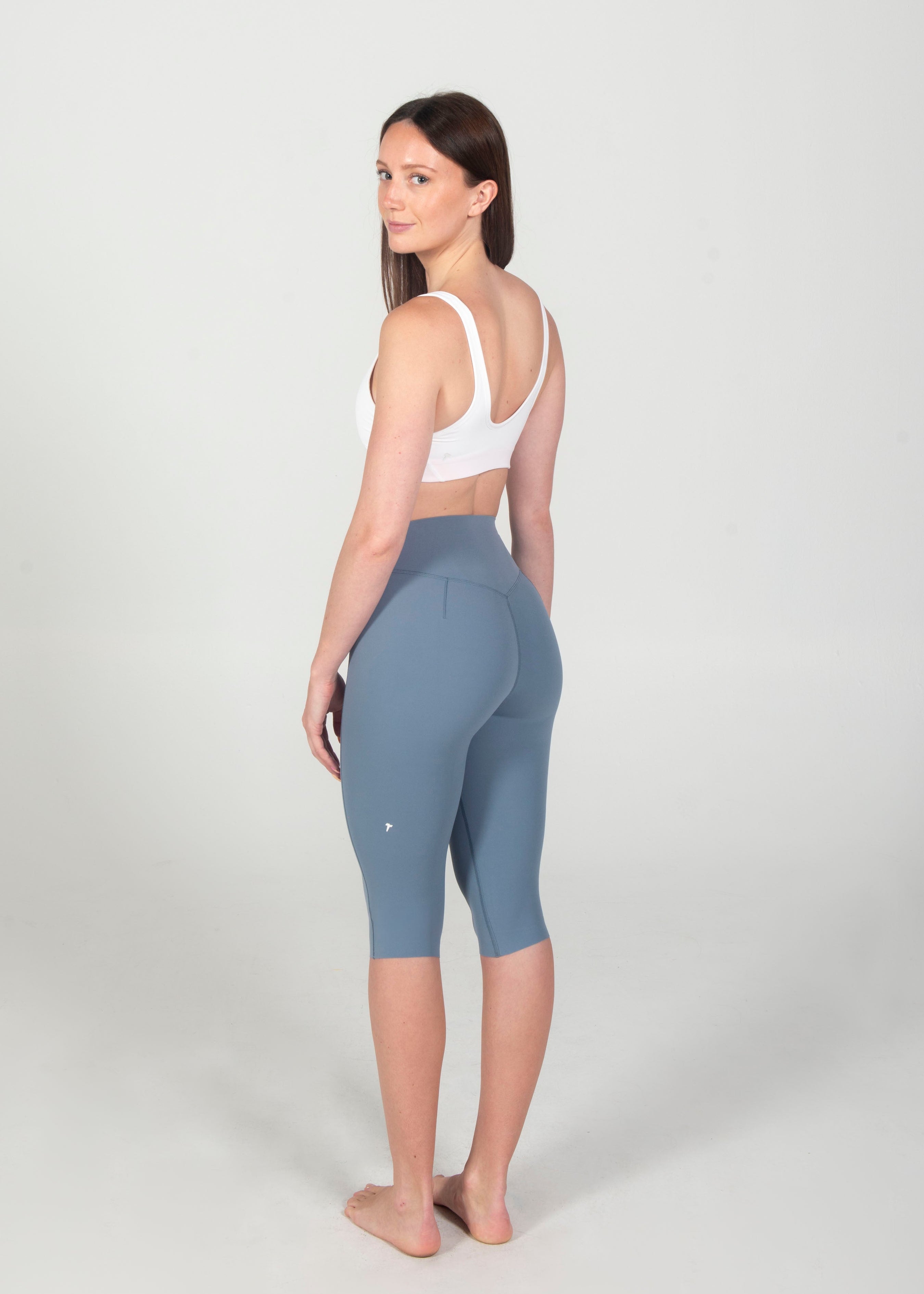 Woman wearing a white sports bra and blue leggings on a white background