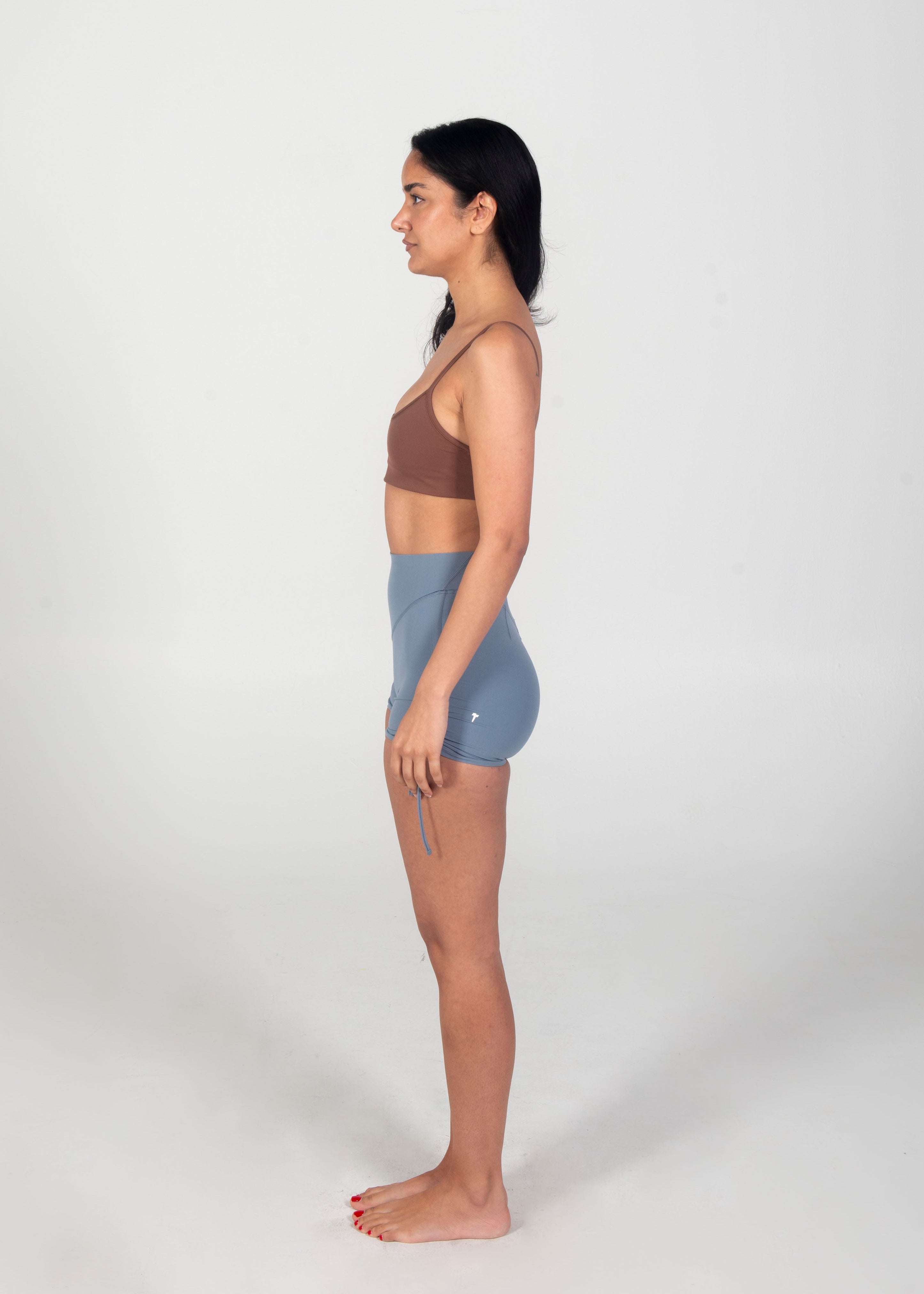 Woman wearing a brown sports bra and blue shorts on a white background