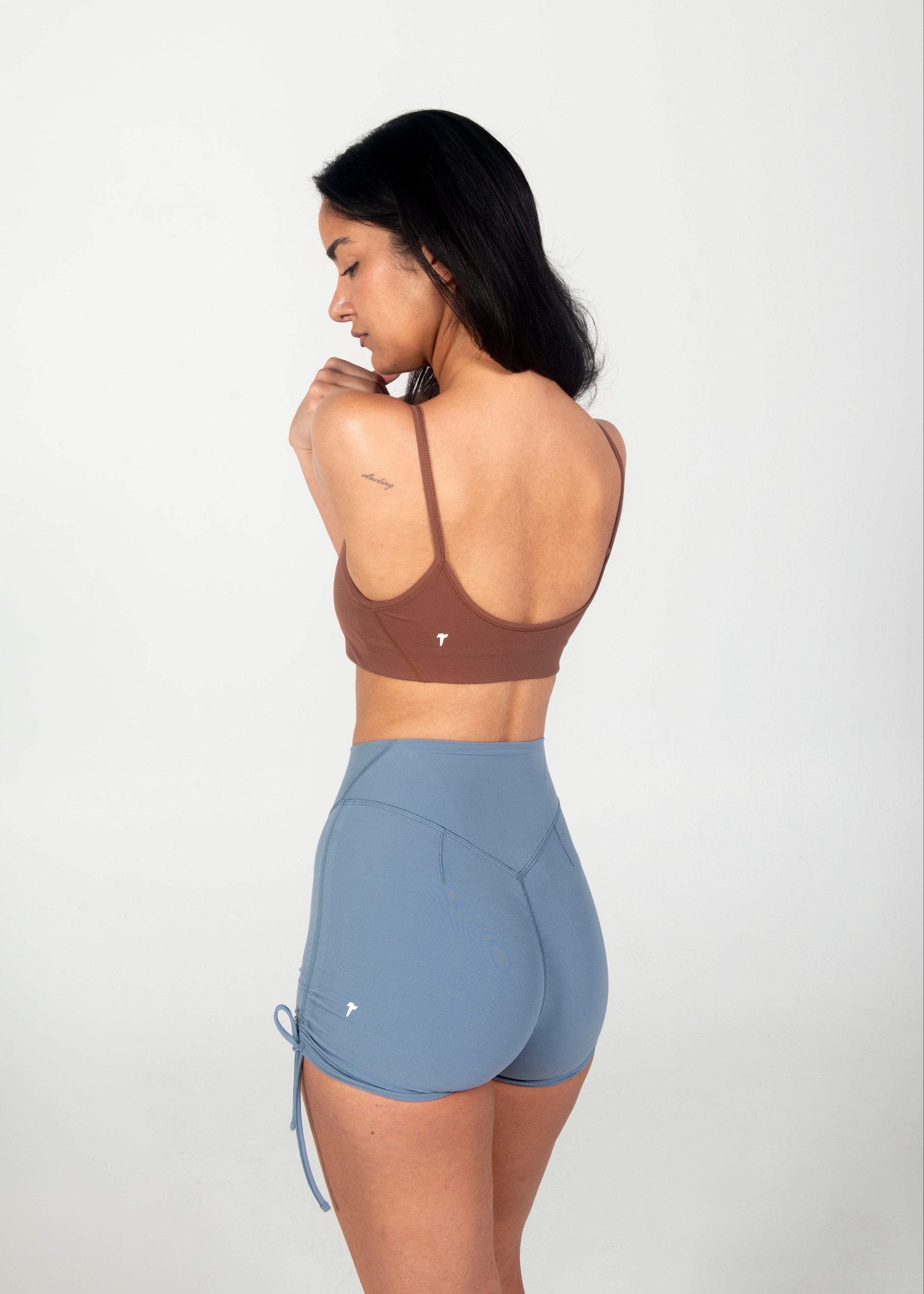 Woman wearing a brown sports bra and blue shorts on a white background
