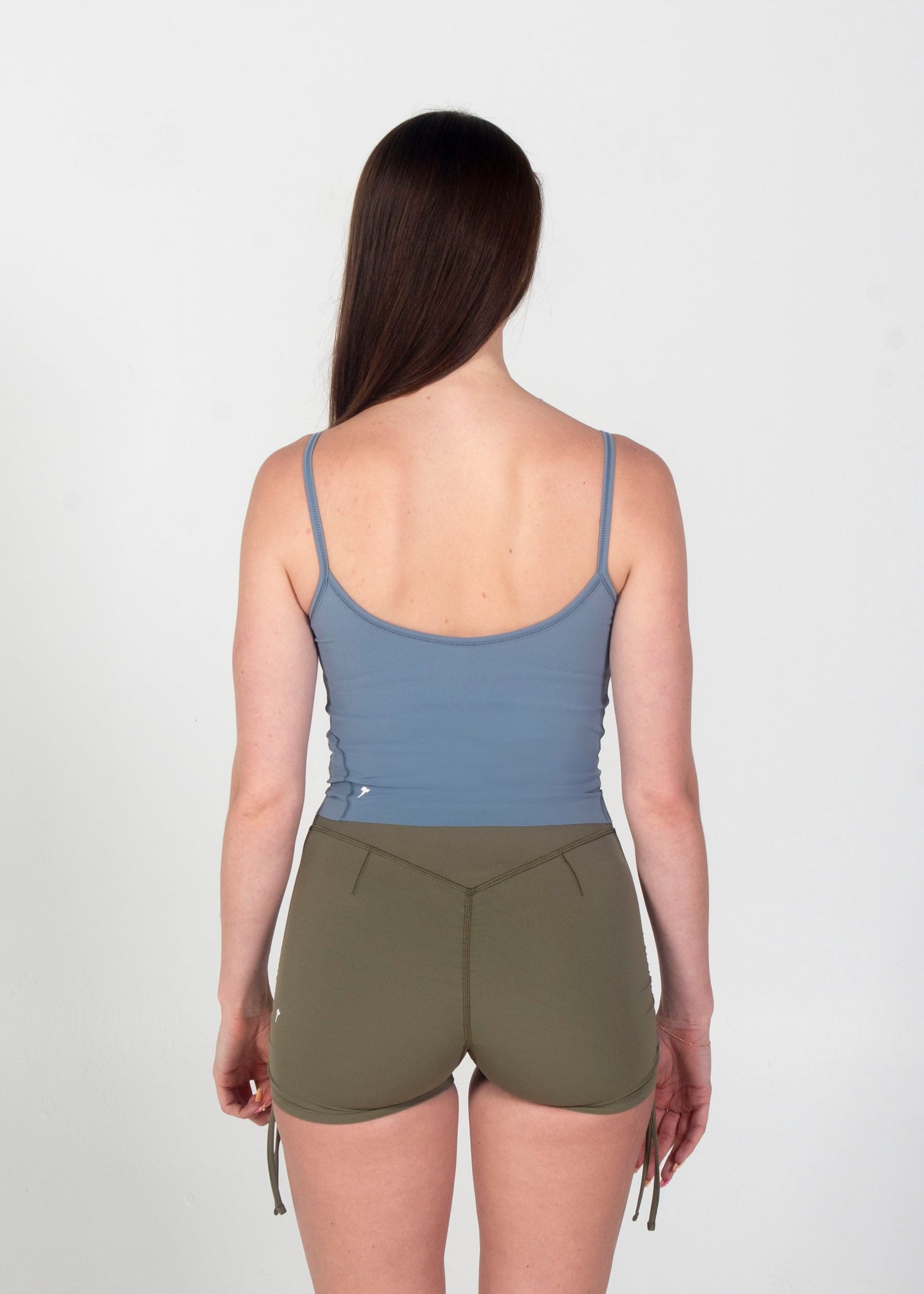 Person wearing a blue tank top and green shorts on a white background