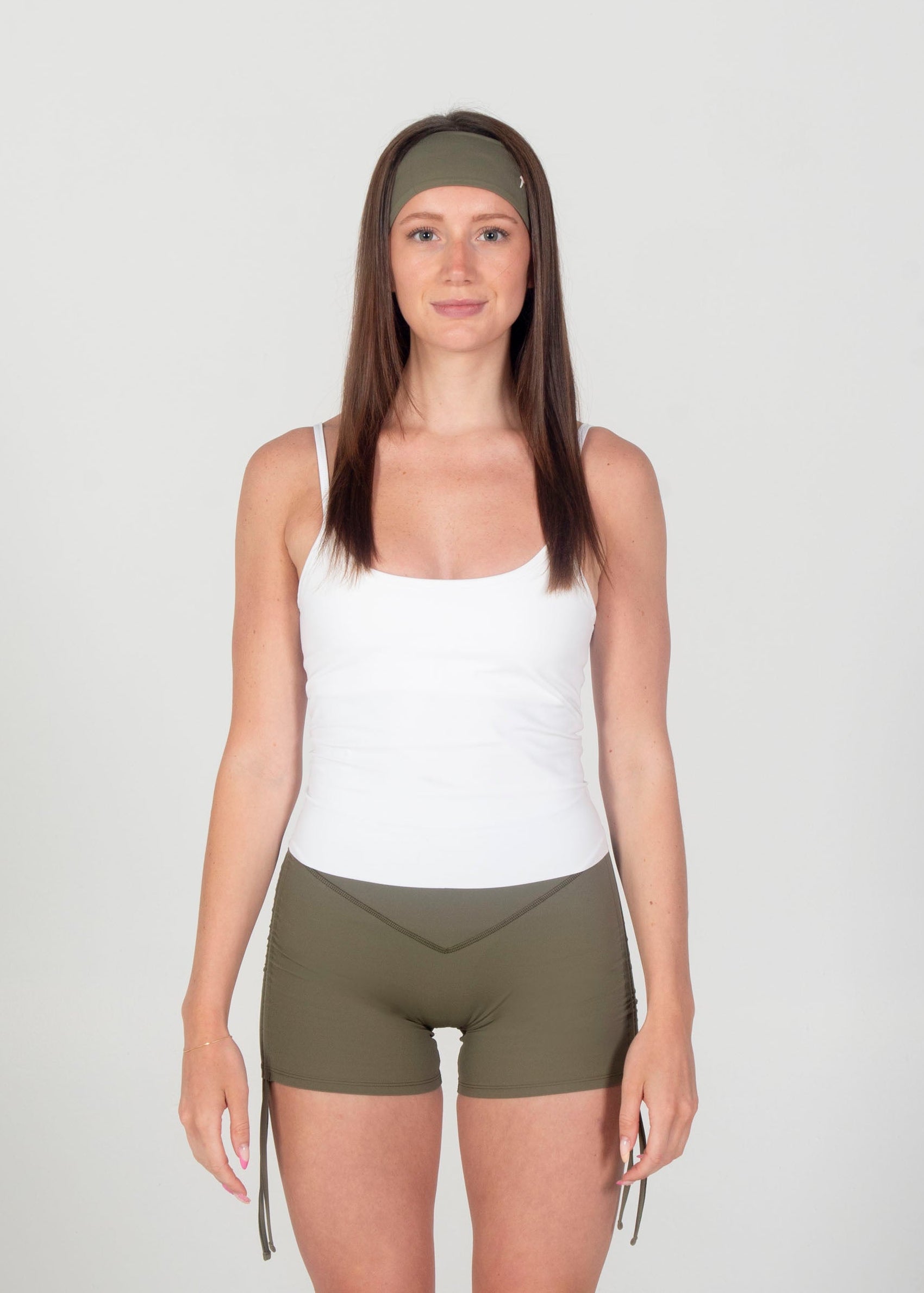 Woman wearing a white tank top and olive green shorts on a plain background