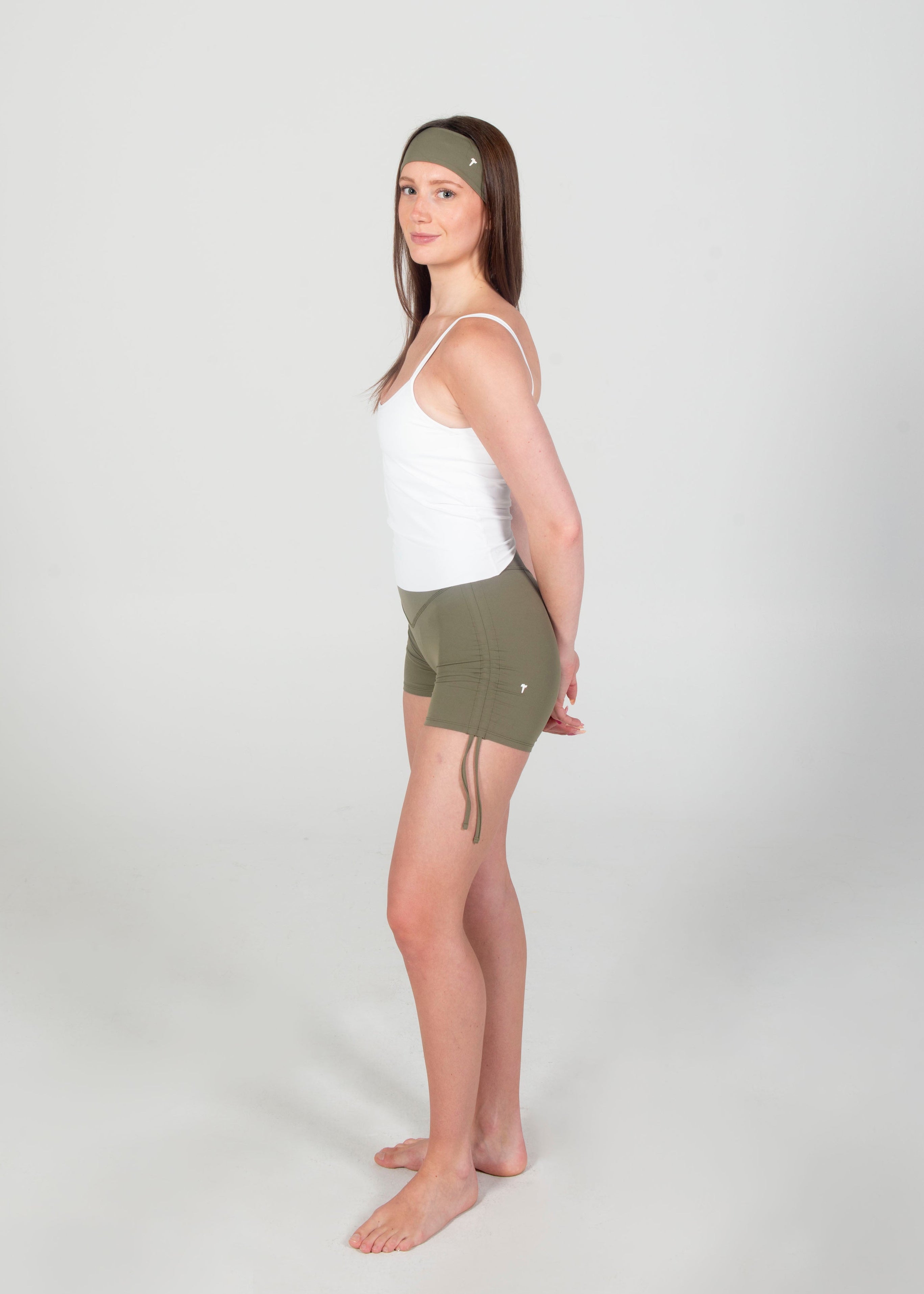 Woman wearing a white tank top and green shorts on a plain background