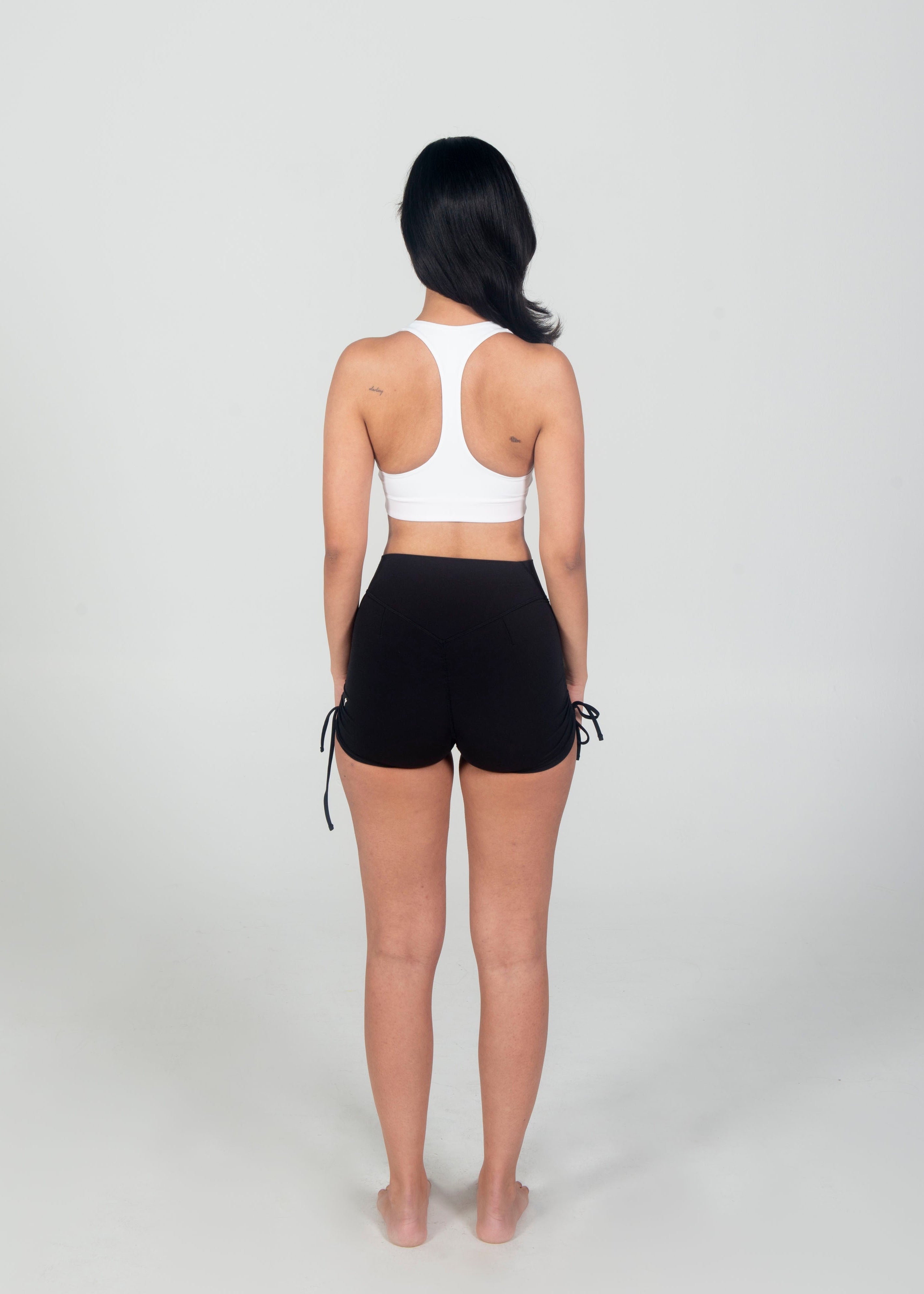 Person wearing a white sports bra and black shorts on a plain background