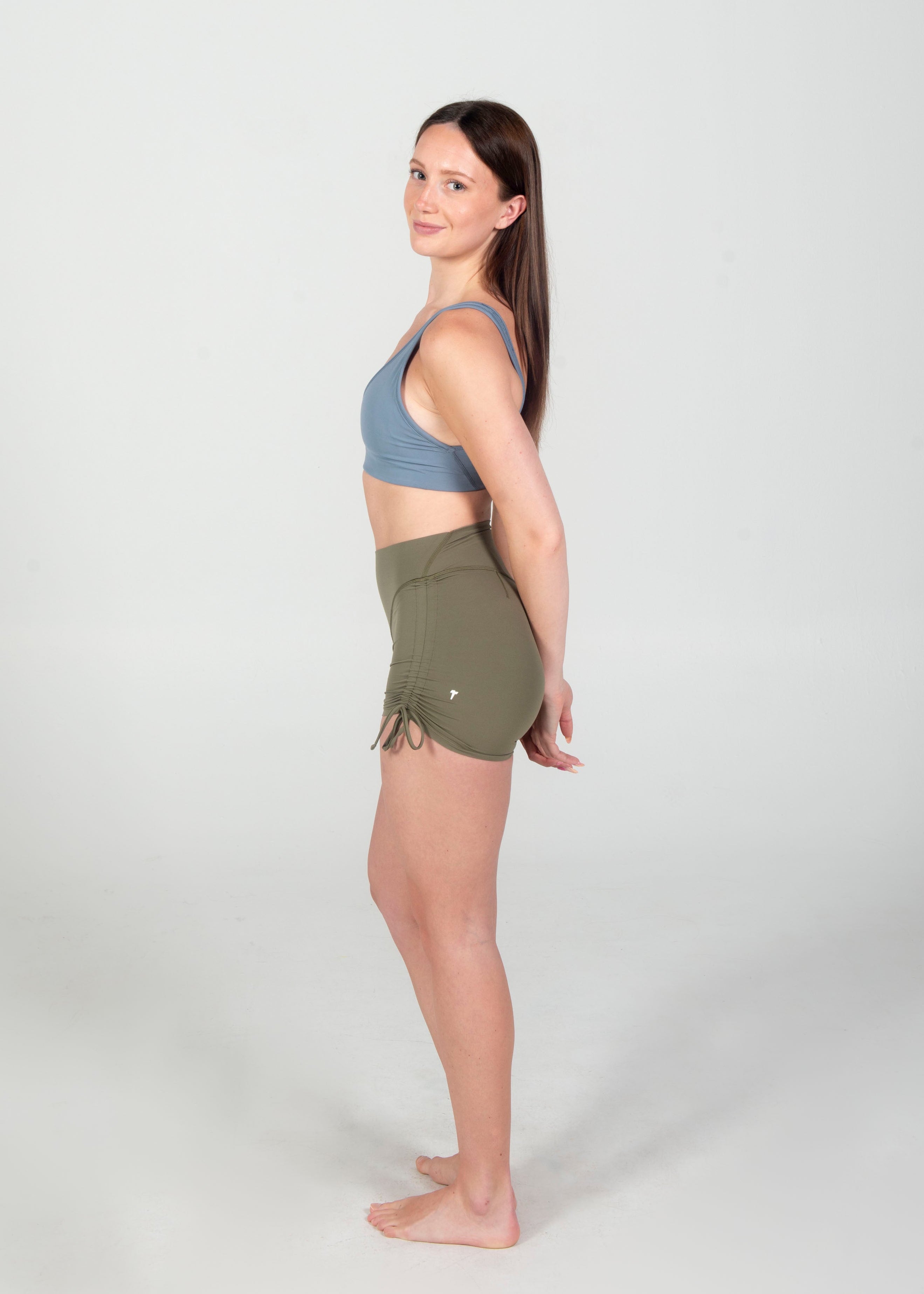 Woman wearing a blue sports bra and green shorts on a white background