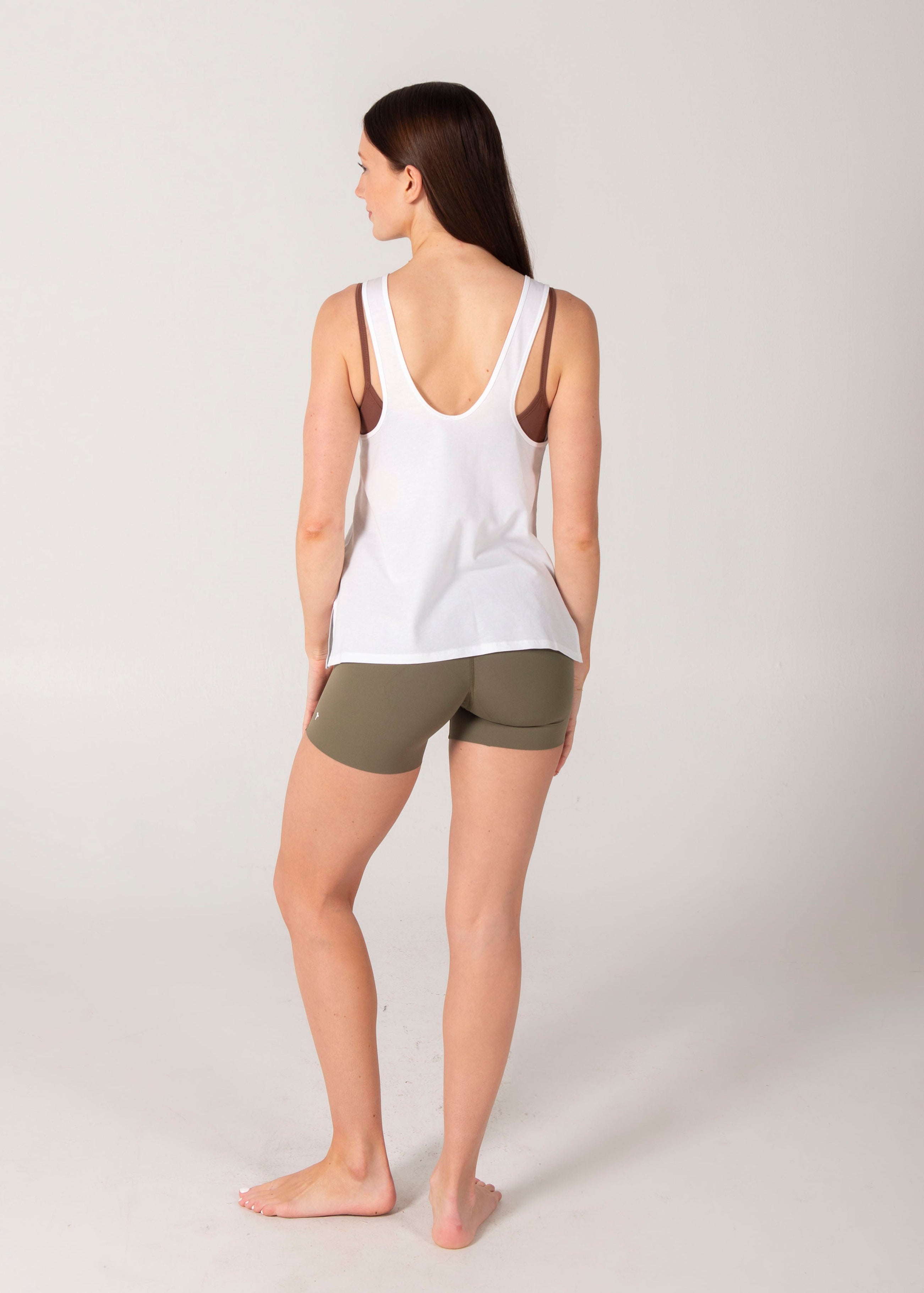 Woman wearing a white tank top and green shorts on a plain background