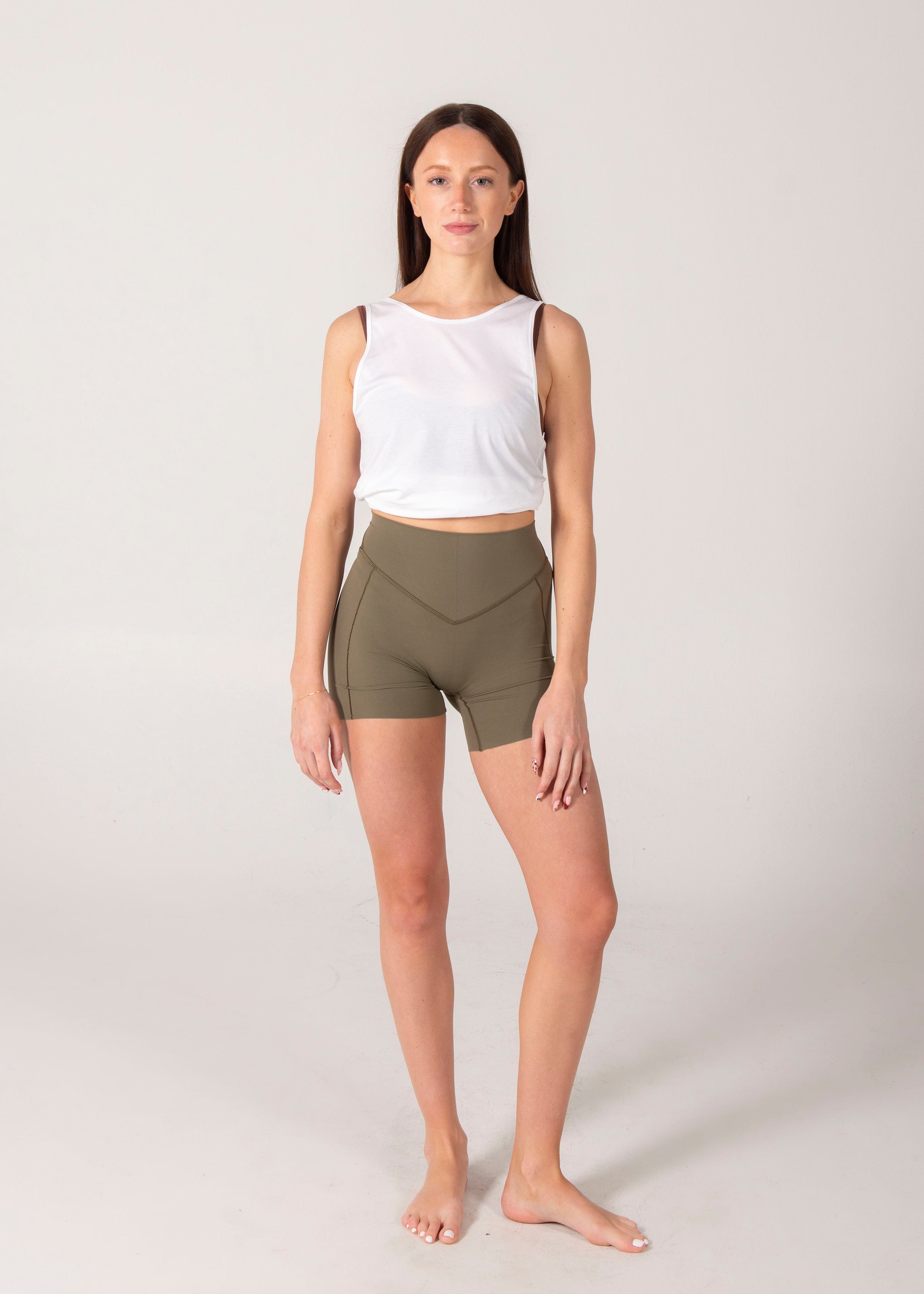 Woman wearing a white tank top and olive green shorts on a light gray background